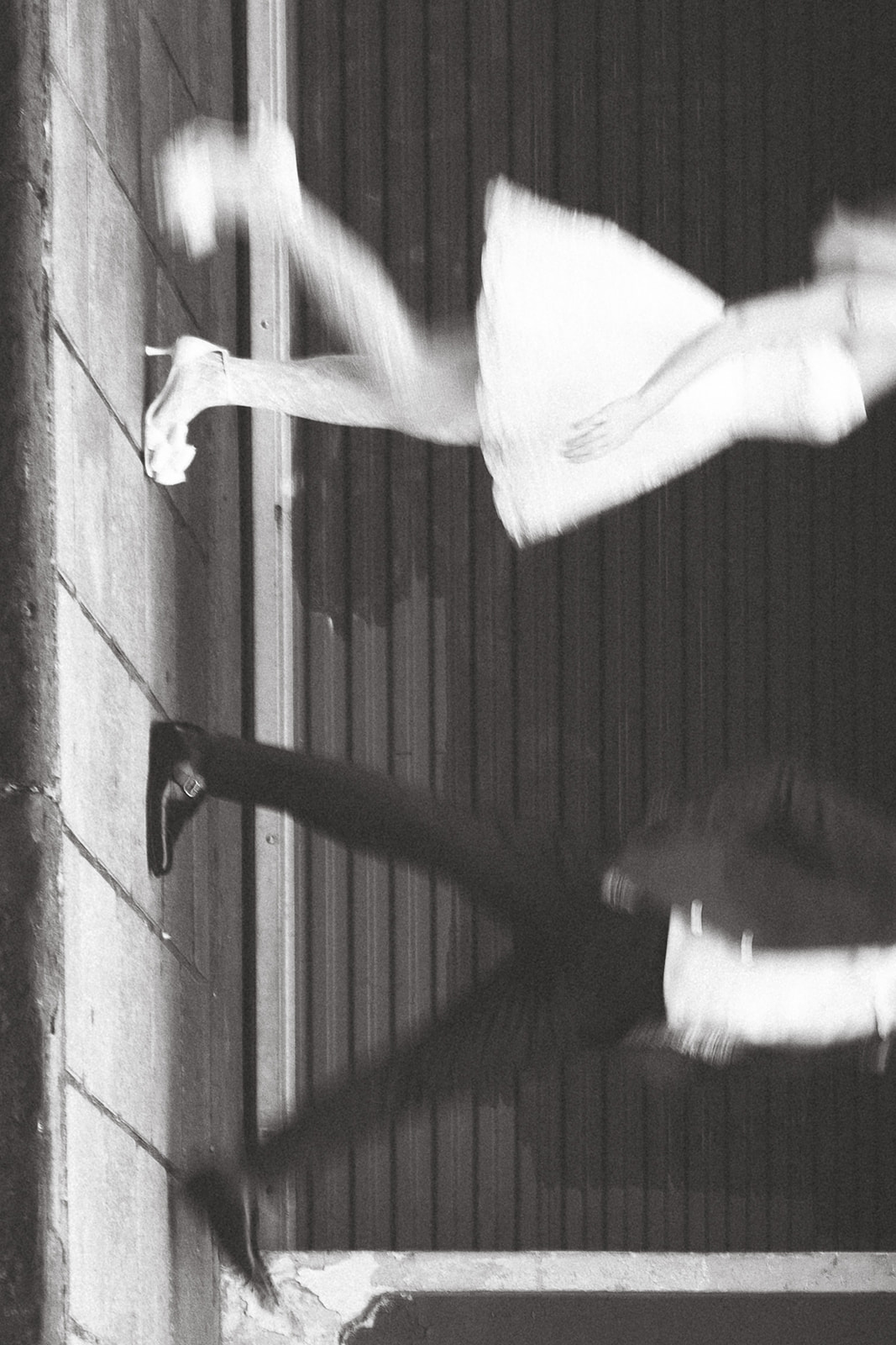 A blurred, motion shot of a couple in a dramatic pose, with their legs extended, capturing a sense of movement and intimacy against an urban backdrop at night.