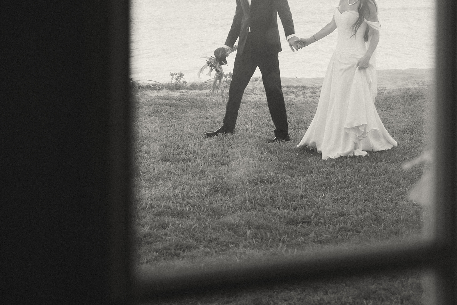 A black and white frame of the couple walking through lush grass near the shoreline, perfectly timeless.
