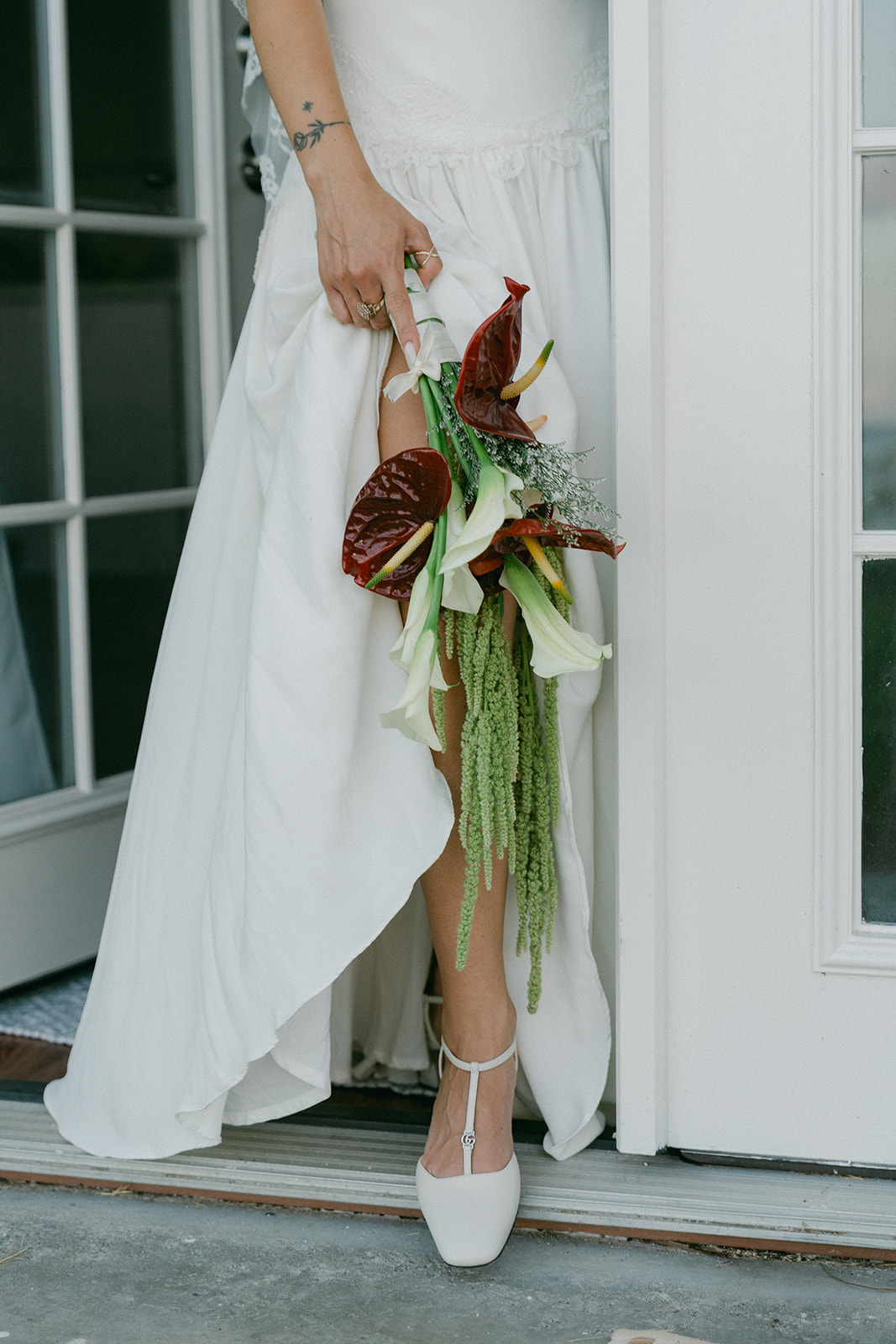 A bride lifting the hem of her gown, revealing sleek white heels and a cascading bouquet of tropical flowers.