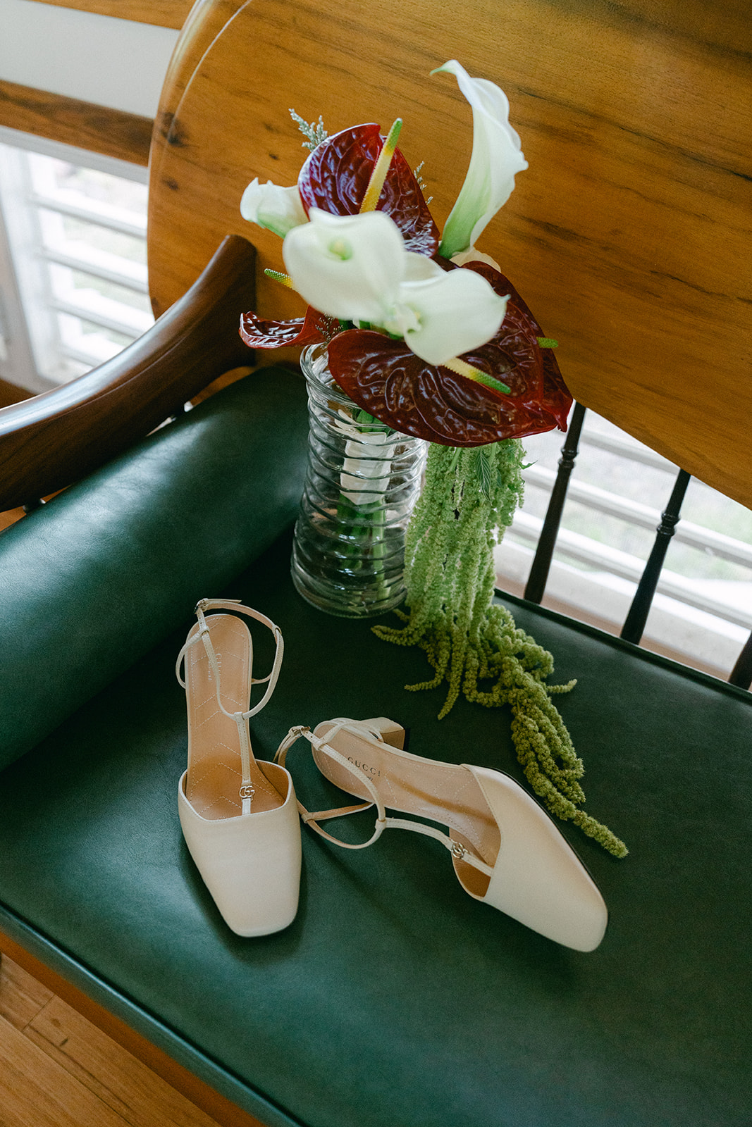 A pair of white heels resting beside a bold red and white tropical bouquet on a green leather bench.