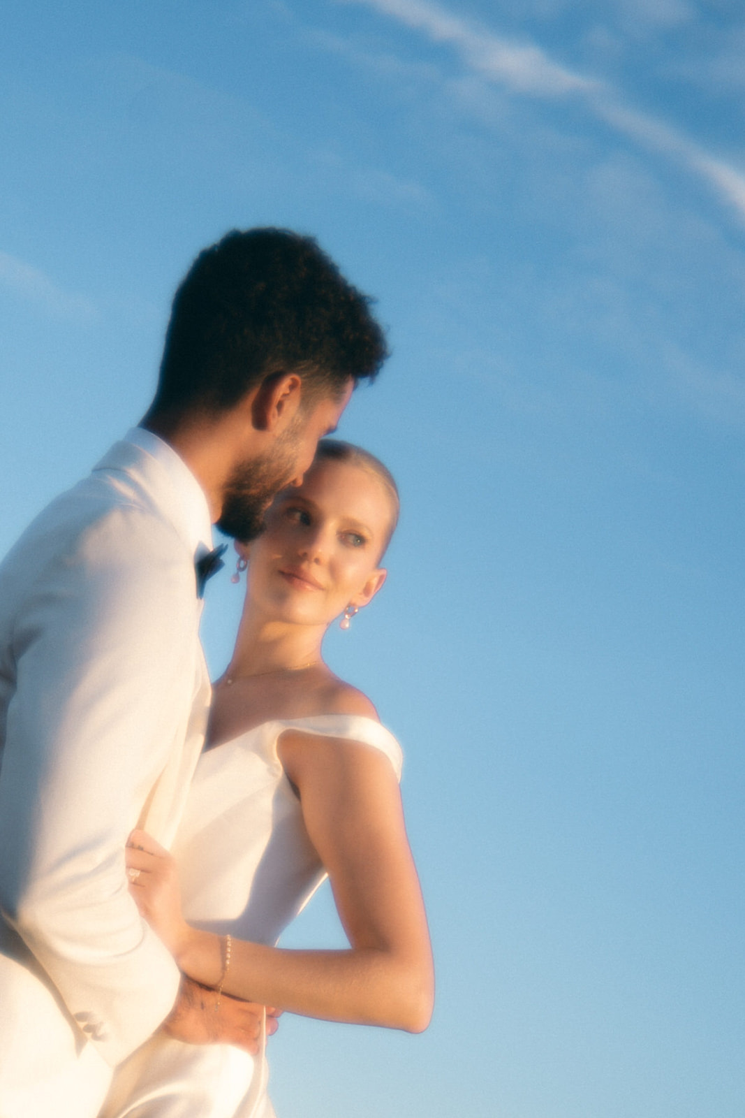  A softly blurred image of a bride and groom embracing under an expansive blue sky, evoking a timeless and dreamy atmosphere.