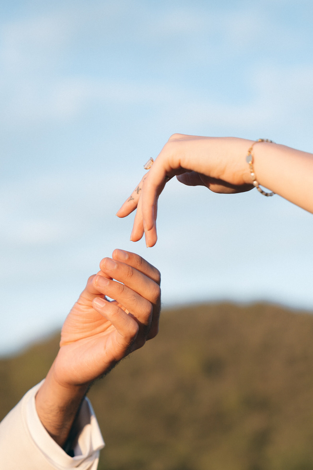 A close-up of two hands gently reaching for each other, set against a natural landscape, capturing a quiet, intimate moment.