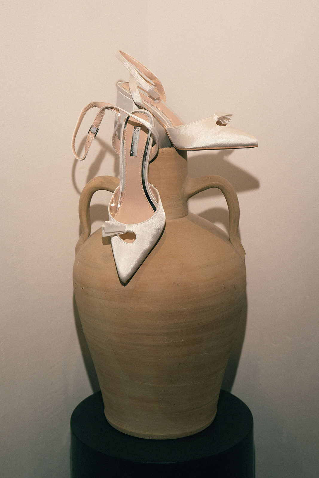 Satin white bridal heels resting on a rustic clay pot, with the soft lighting highlighting the shoes.