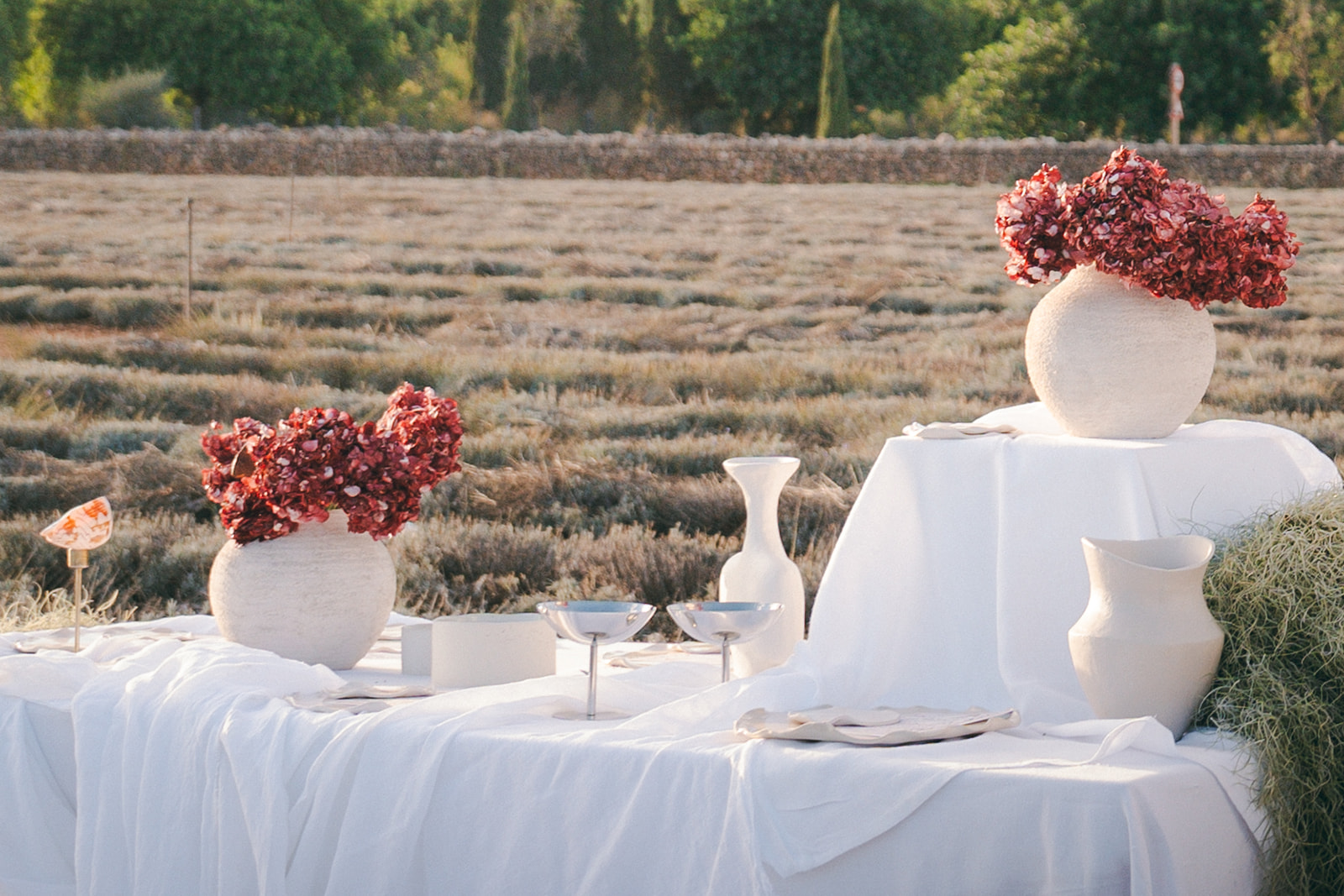 A wedding setup featuring floral arrangements in large vases, with a white tablecloth and a view of a beautiful outdoor landscape.