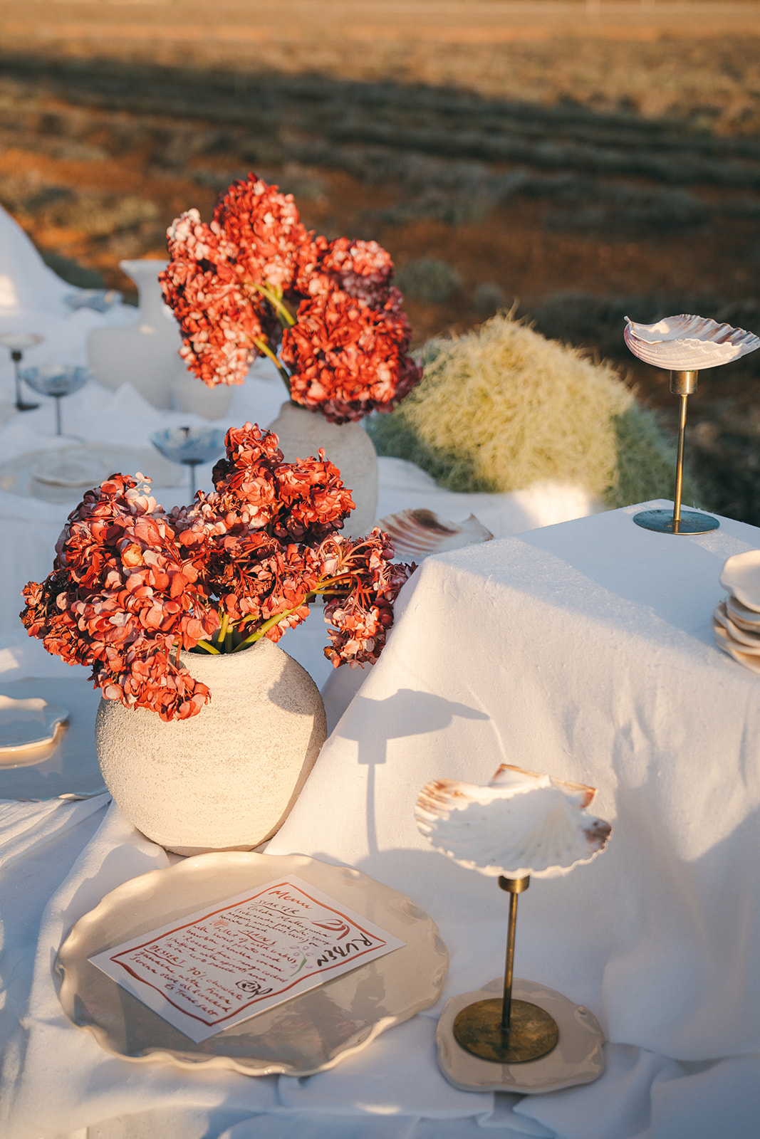 A close-up of a wedding reception table, decorated with sculptural floral arrangements, shell-inspired tableware, and handwritten place cards.