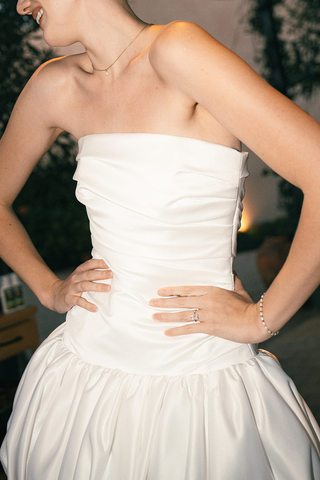 A cropped shot of a bride’s wedding dress, highlighting the structured bodice, soft ruching, and her delicate jewelry.