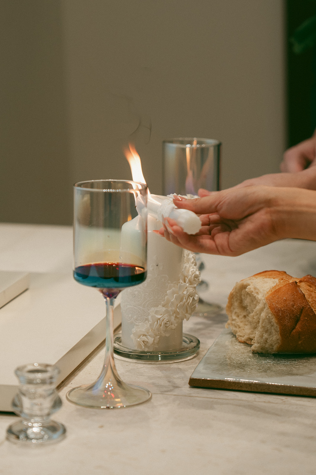 A close-up of a unity candle being lit during a wedding ceremony, with a glass of wine and a loaf of bread symbolizing a communion ritual.