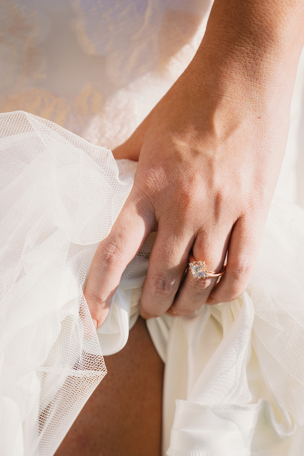 A close-up of the bride adjusting her wedding dress, highlighting her engagement ring.