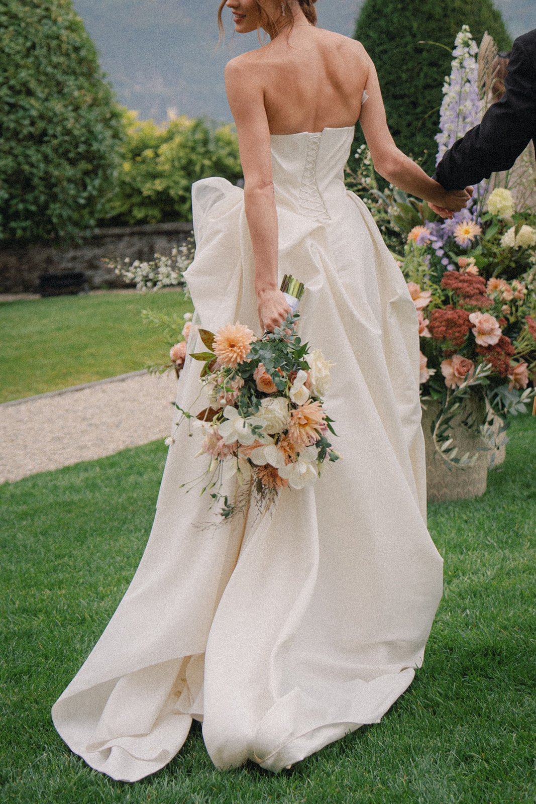 A bride holding her bouquet in one hand while walking away, with the flowing train of her dress cascading behind her.