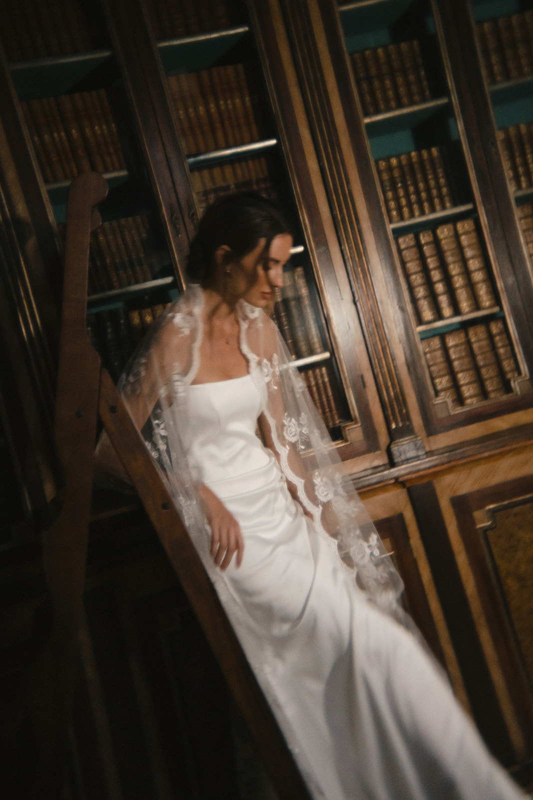 Bride descending a library ladder, draped in a lace veil, adding a timeless touch to Bridal Photography in Hawaii.