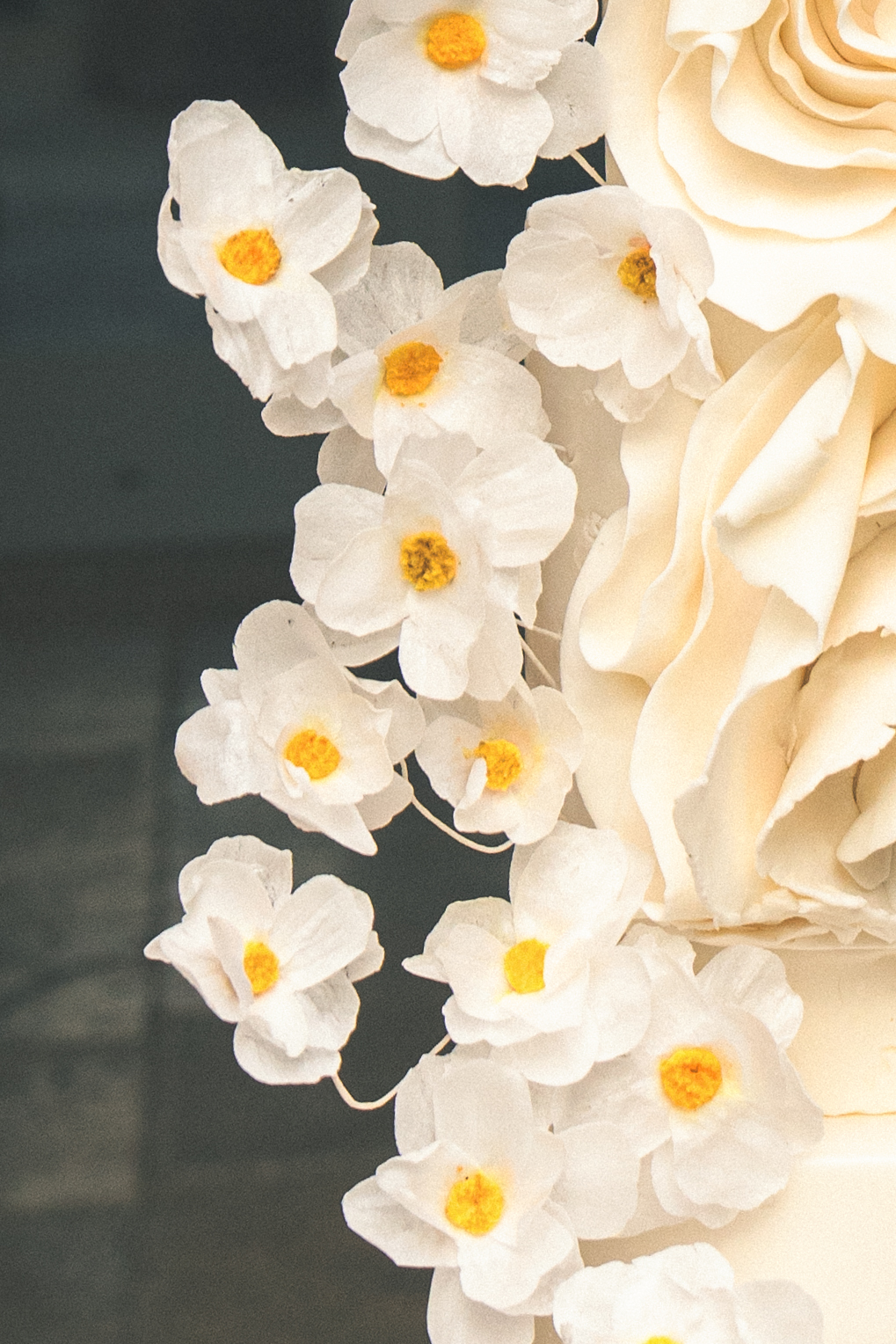 A close-up of an elegant wedding cake decorated with delicate white sugar flowers with yellow centers, arranged artistically alongside creamy sculpted icing.