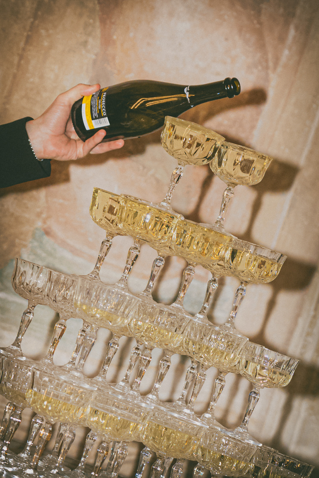 A celebratory moment of champagne being poured into a multi-tiered coupe glass tower, capturing the festive energy of a wedding reception.