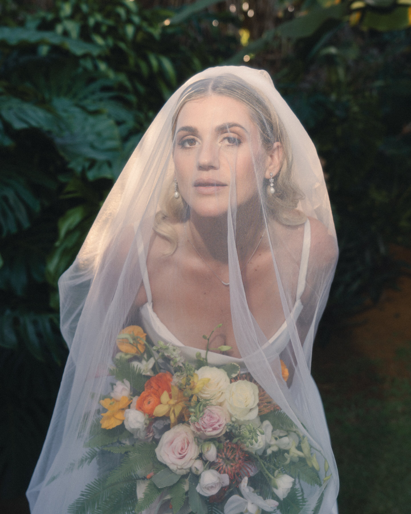 A bride gazes through her veil while holding a lush, colorful bouquet of tropical flowers—evoking natural beauty in this Destination Wedding Photography Guide for Couples Planning a Hawaii Wedding.