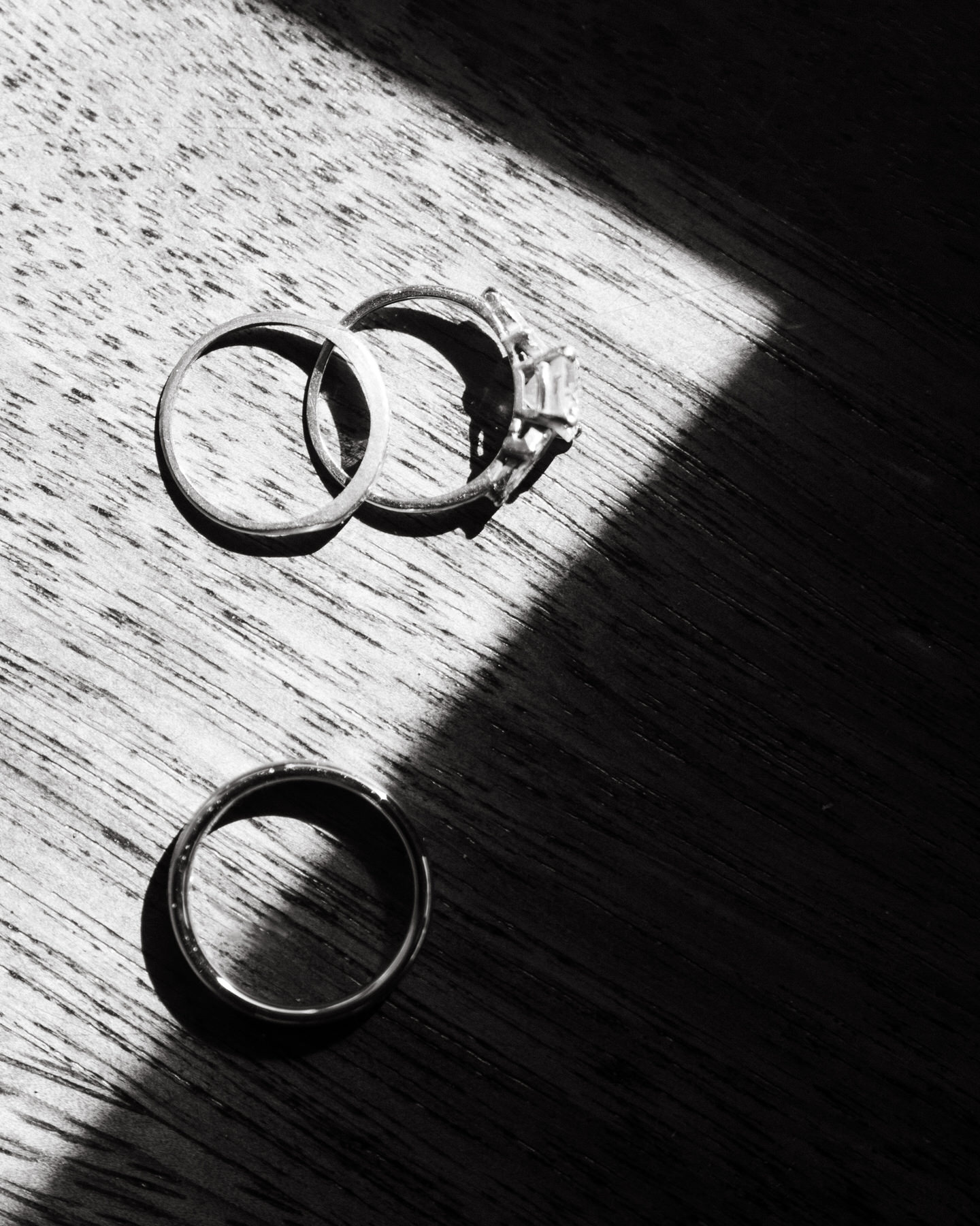 Three wedding rings, including a solitaire diamond, rest in dappled sunlight on wood—classic flat-lay detail from a Destination Wedding Photography Guide for Couples Planning a Hawaii Wedding.