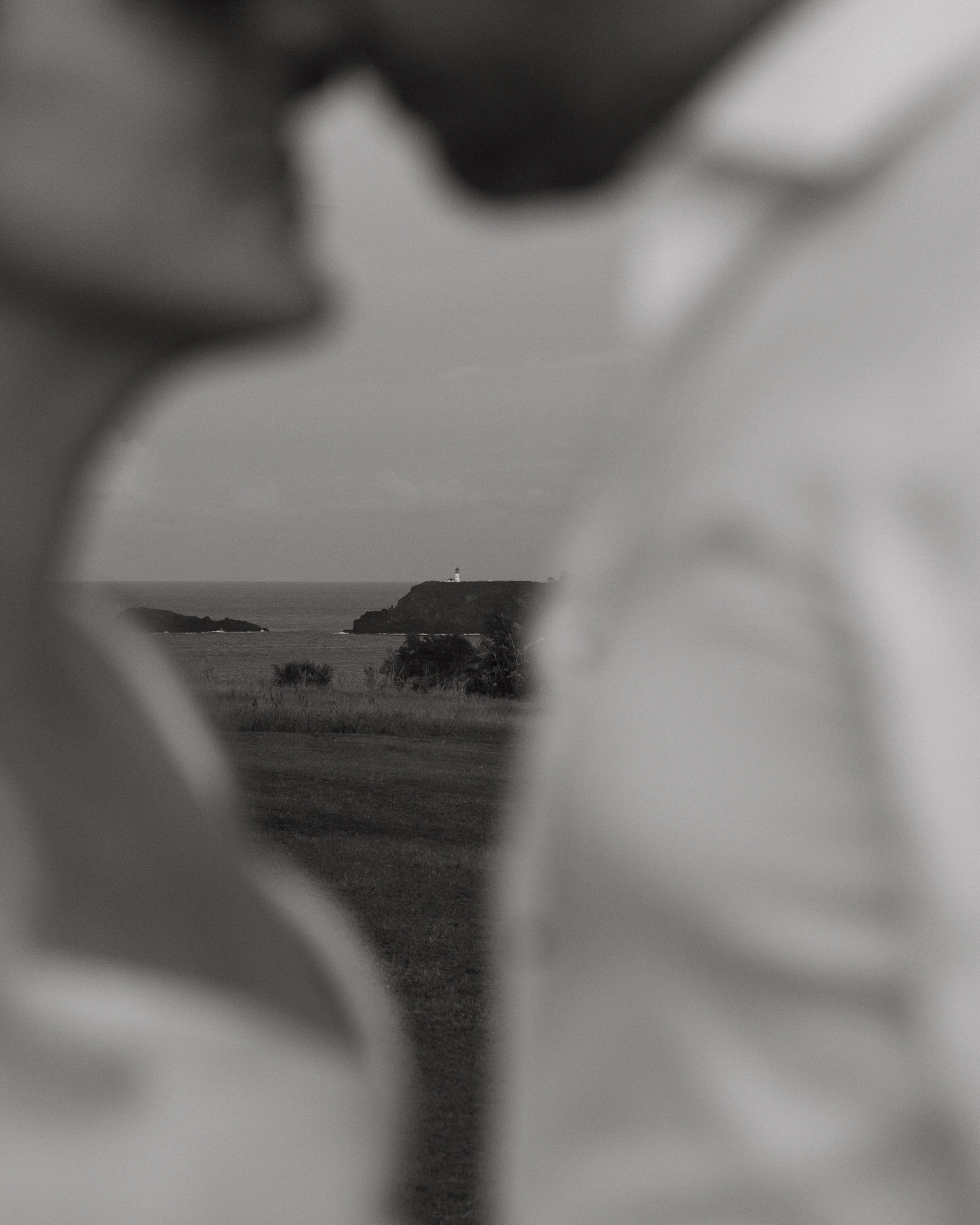 A distant lighthouse on a coastal cliff is framed by the out-of-focus silhouettes of a couple, adding storytelling magic to a Destination Wedding Photography Guide for Couples Planning a Hawaii Wedding.