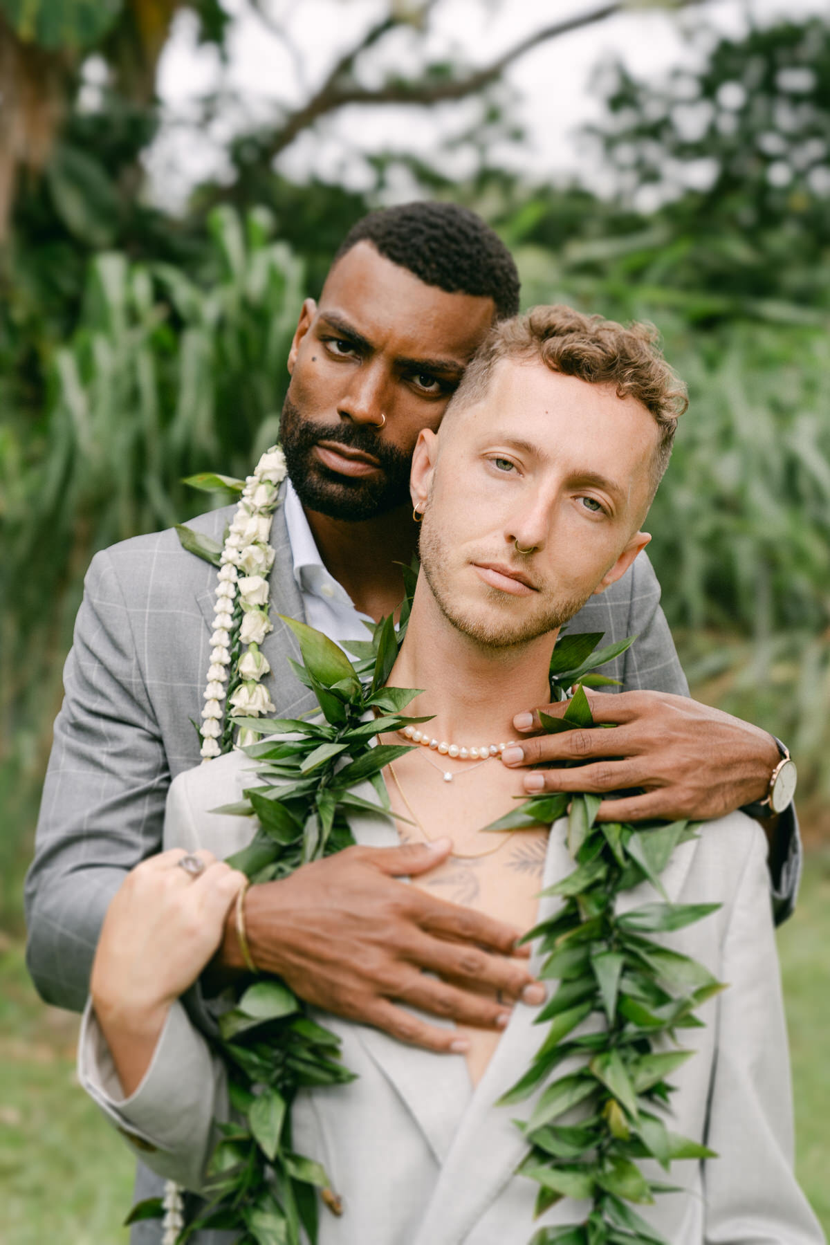 Two grooms embracing in a lush Hawaiian landscape, adorned with traditional lei, captured in Elopement Photography in Hawaii.