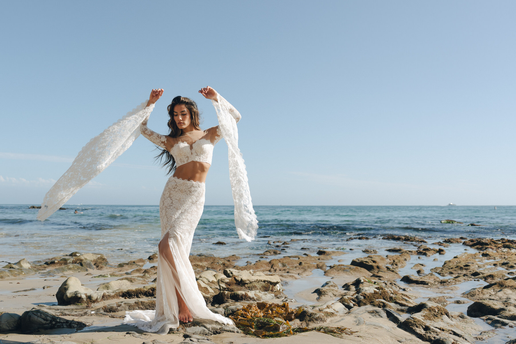 Bride wearing a bohemian-inspired lace wedding dress, dancing on the beach with a clear sky and ocean in the background in Elopement Photography in Hawaii.