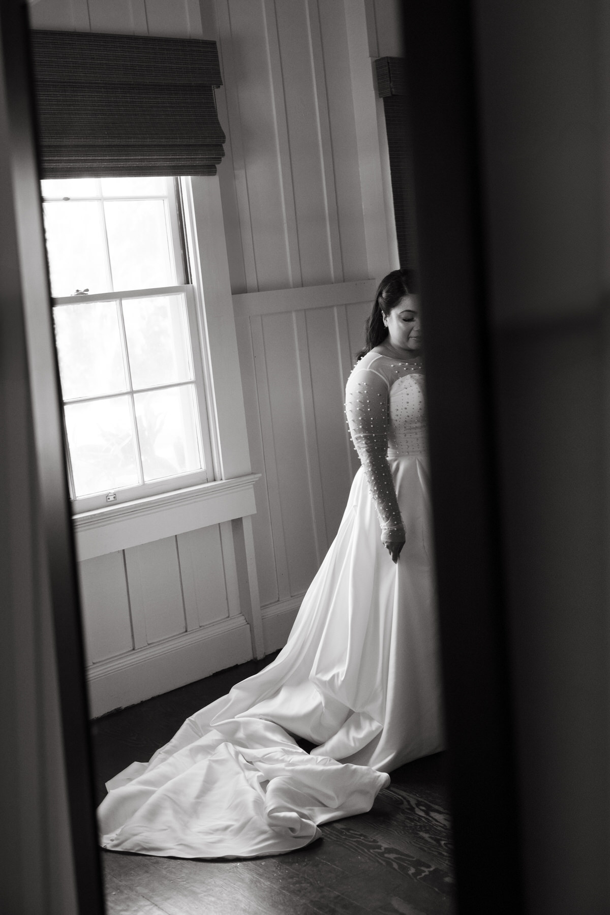 In a quiet moment, a bride in a pearl-detailed gown stands beside a window, the soft lighting adding emotional depth to this image featured in a Destination Wedding Photography Guide for Couples Planning a Hawaii Wedding.