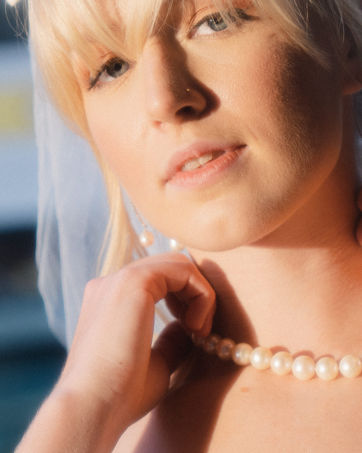 Bride adjusting her pearl necklace on her wedding day, captured in soft light for a timeless bridal portrait in Bridal Photography in Hawaii.