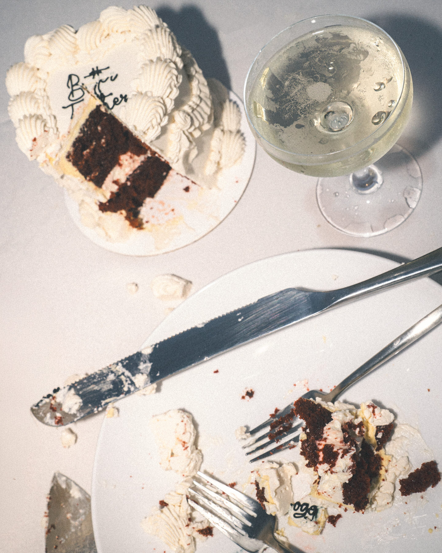 A close-up shot of a partially eaten cake with the words "Better Together" written on the icing. A glass of champagne sits next to the cake, and the plate holds a slice of cake with crumbs and frosting, capturing a moment of celebration captured by Masha Photo.