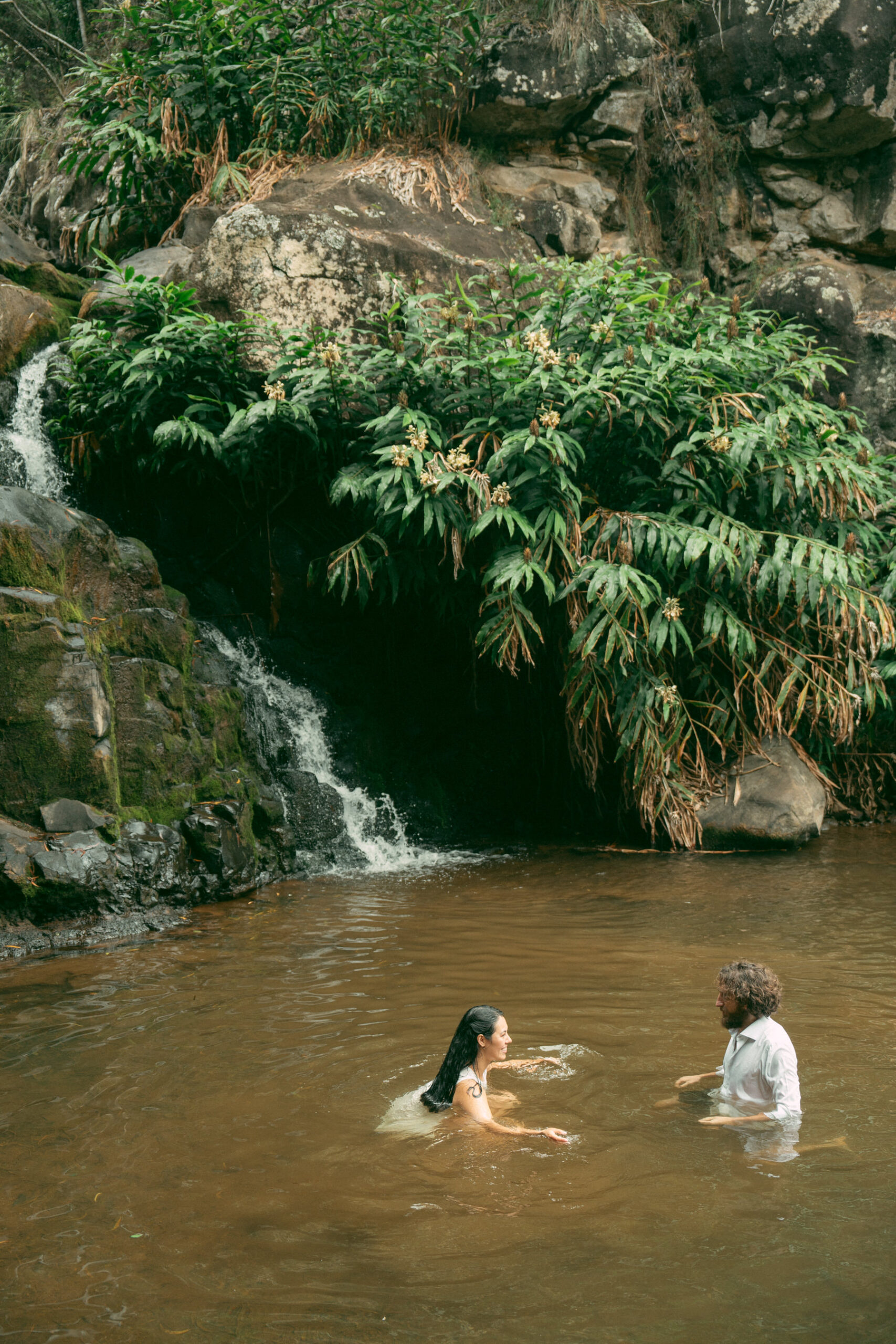 Couple in an intimate moment in a natural waterfall pool, showcasing the raw beauty of their elopement in Elopement Photography in Hawaii.