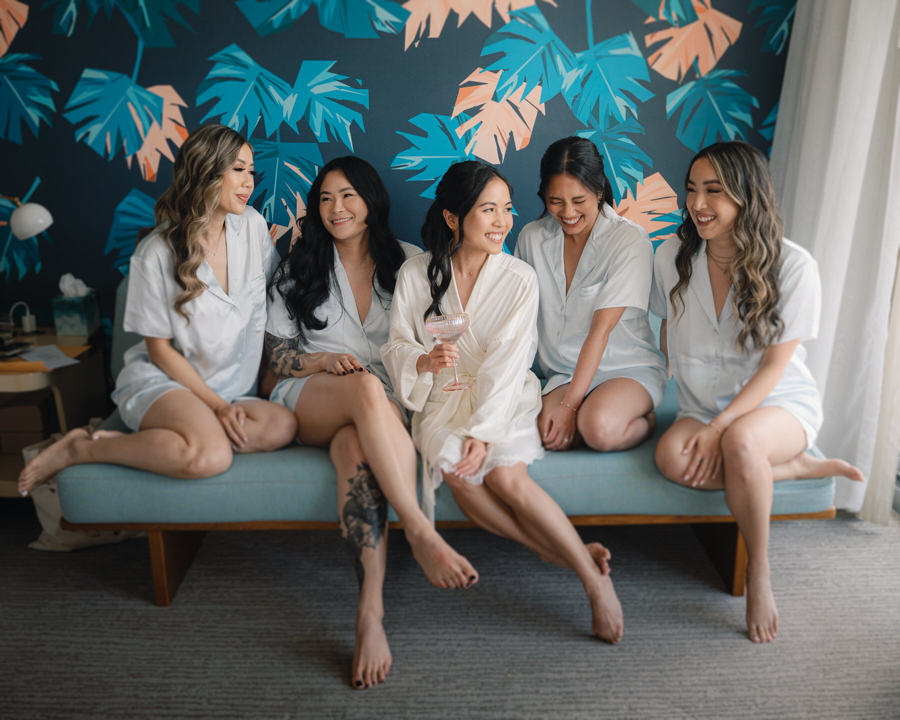 The bride and her bridesmaids share a cozy moment in matching satin pajamas, lounging on a mid-century bench—morning-of joy in La Pietra Wedding: A Guide for Modern Couples.