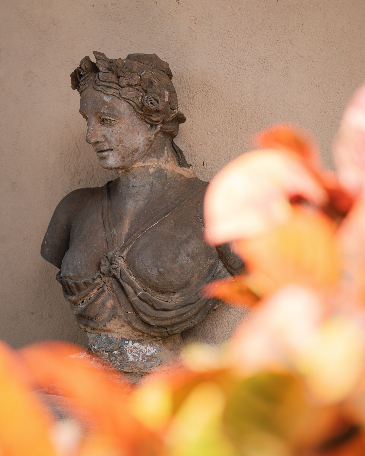 A weathered stone bust of a woman with a flower crown peeks out behind vibrant orange leaves—capturing the artistic ambiance of La Pietra Wedding: A Guide for Modern Couples.