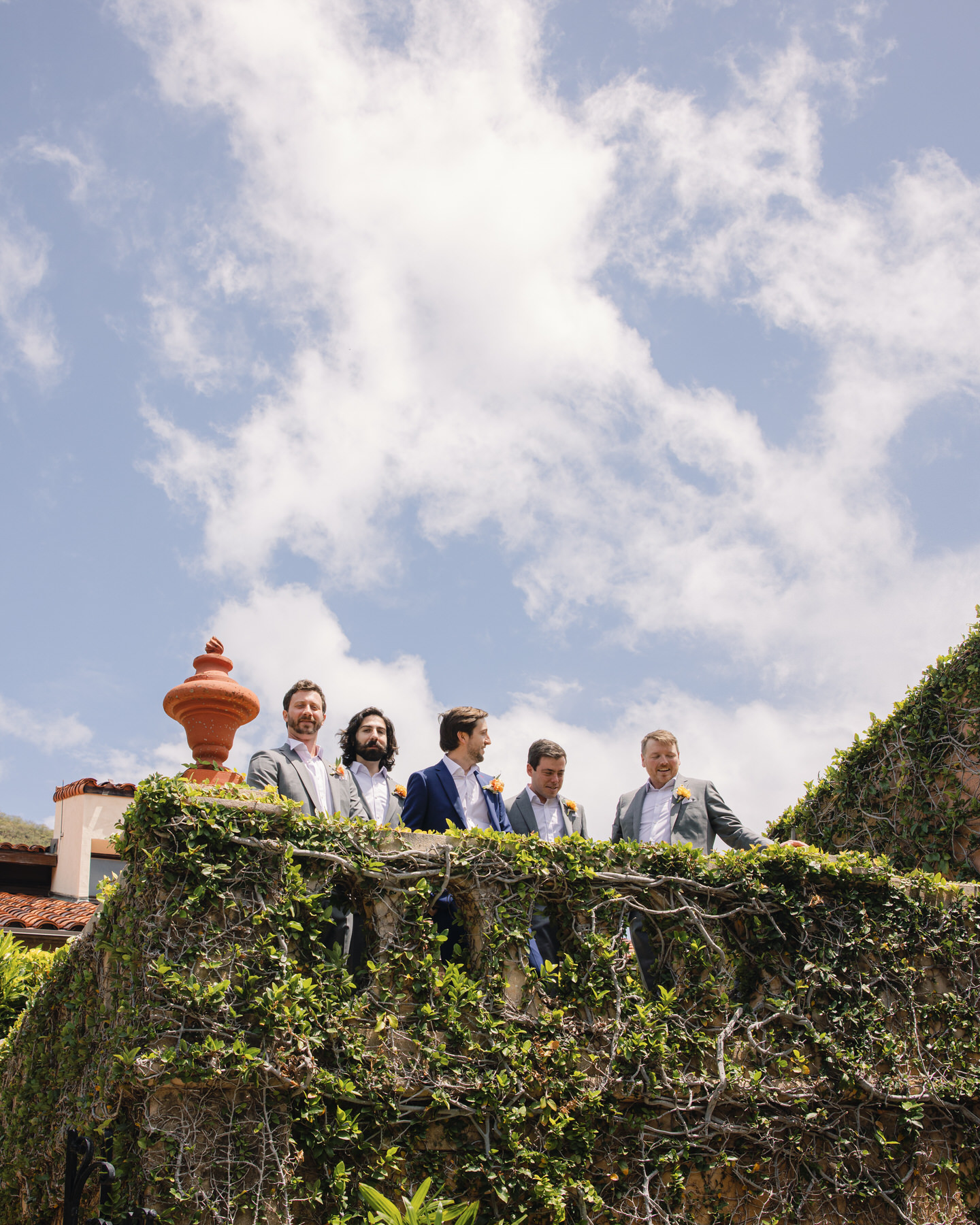 The groom and his groomsmen stand atop a vine-covered terrace at La Pietra, laughing under a bright blue sky—modern camaraderie captured for La Pietra Wedding: A Guide for Modern Couples.