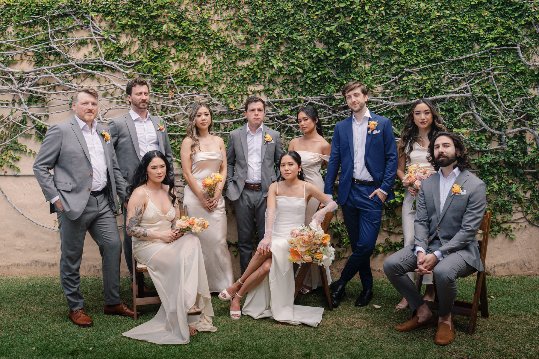 A modern wedding party poses with confidence against a vine-draped wall, dressed in neutral tones with peach and yellow florals—elevated squad goals for La Pietra Wedding: A Guide for Modern Couples.