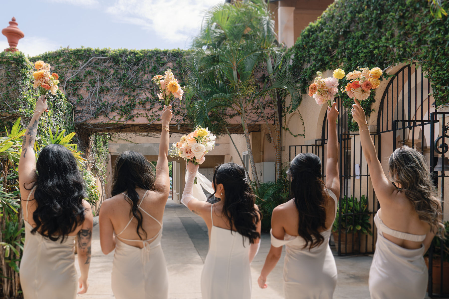 A joyful lineup of bridesmaids and the bride, all in soft ivory gowns, hold their bouquets high under the vine-covered archways—celebrating unity and style in La Pietra Wedding: A Guide for Modern Couples.