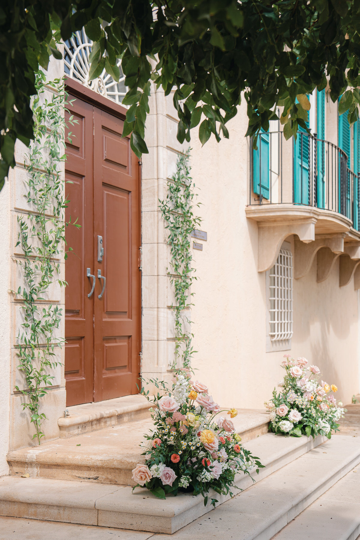 Elegant floral arrangements in soft blush and citrus tones frame the front door of La Pietra’s villa—charming ceremony setup from La Pietra Wedding: A Guide for Modern Couples.
