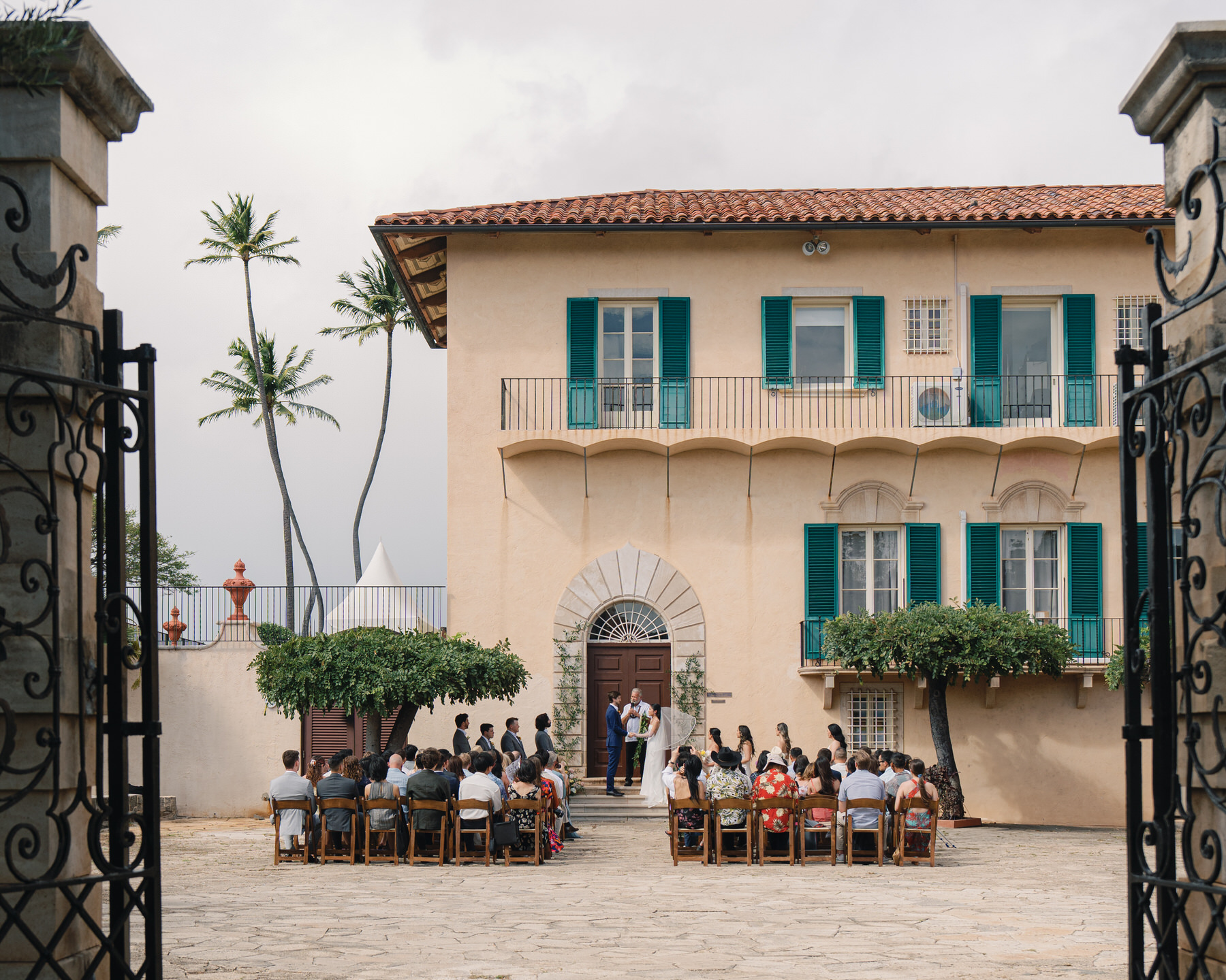 A wedding ceremony in progress on the stone courtyard at La Pietra, with the couple exchanging vows before guests seated under swaying palm trees—an essential scene in La Pietra Wedding: A Guide for Modern Couples.