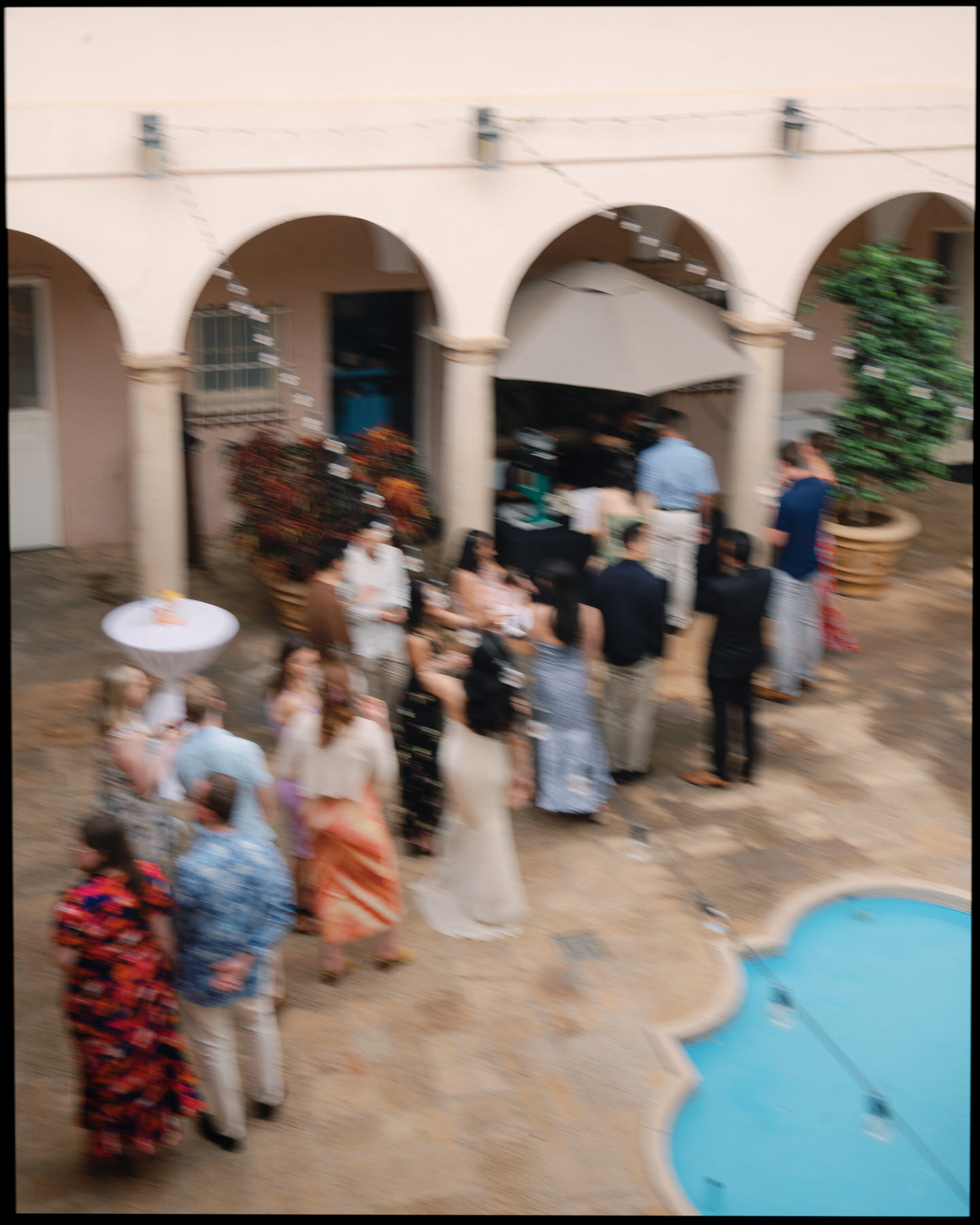 A lively wedding cocktail hour with guests mingling around a pool in the Mediterranean-style courtyard at La Pietra, captured in a candid moment for La Pietra Wedding: A Guide for Modern Couples.