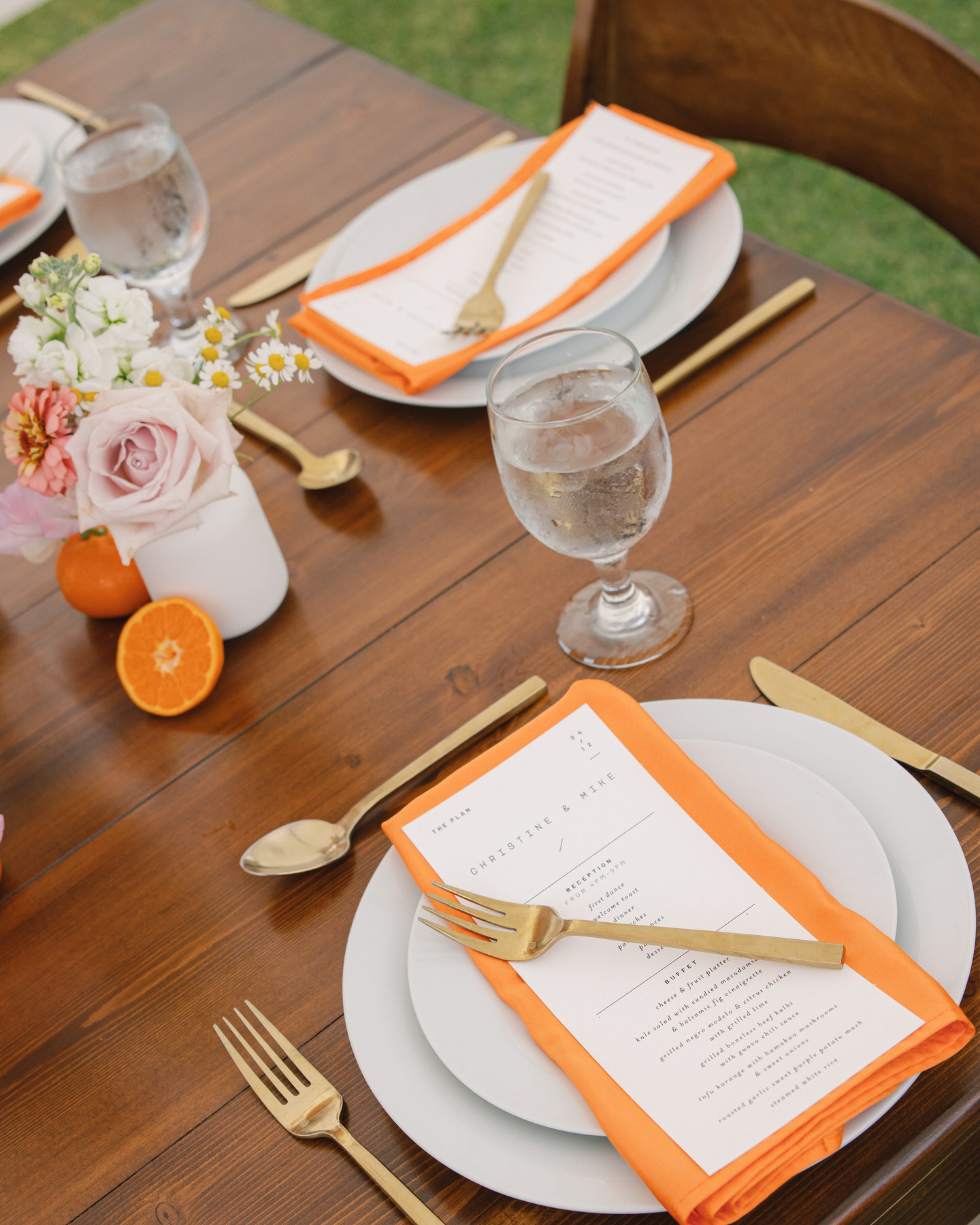 A wedding reception table set with orange-edged menus, gold cutlery, and fresh citrus accents—bold yet refined design from La Pietra Wedding: A Guide for Modern Couples.