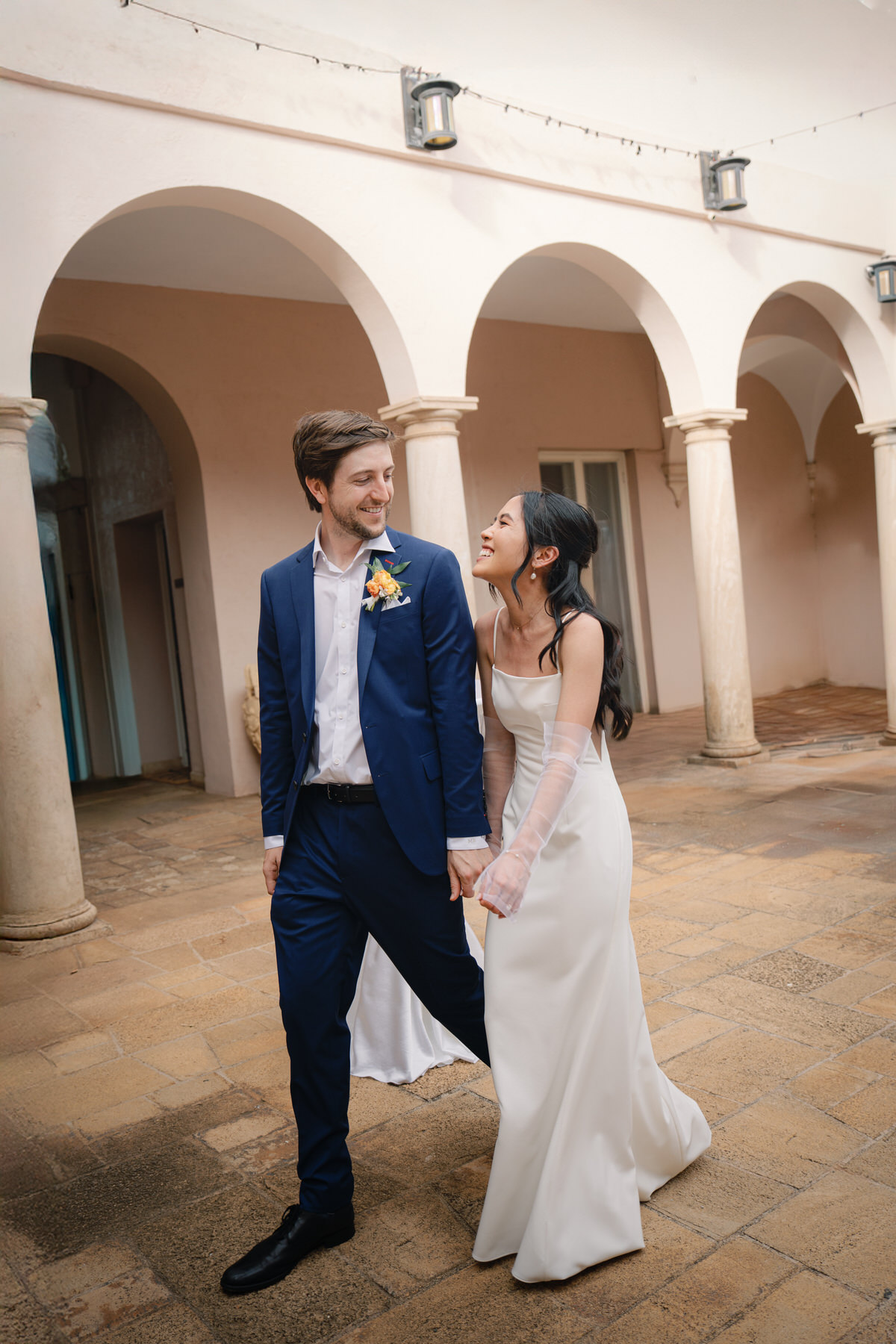 A newlywed couple walks hand-in-hand through La Pietra’s courtyard arches, glowing with happiness—pure joy featured in La Pietra Wedding: A Guide for Modern Couples.