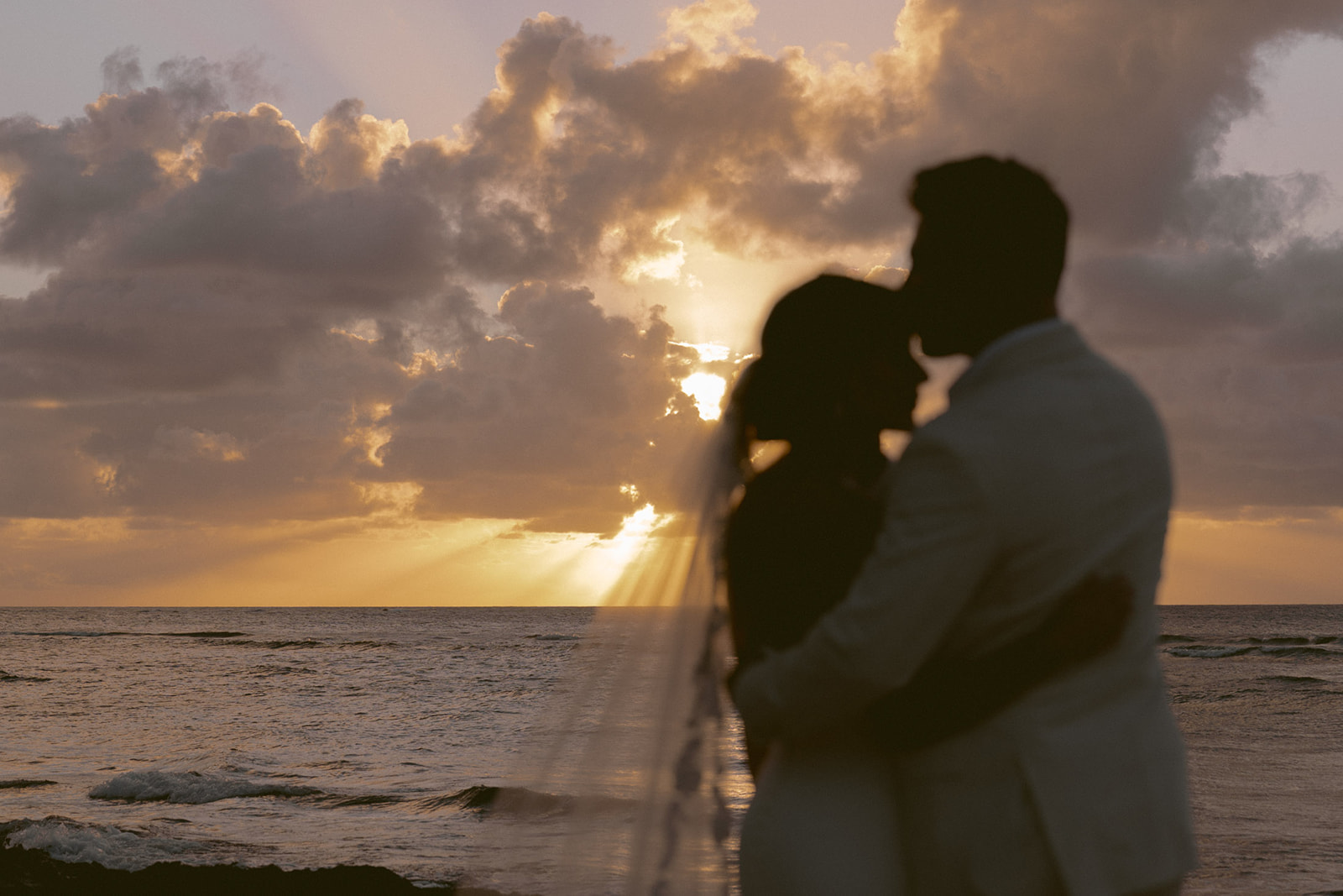 Couple sharing a kiss at sunset on the beach during their marriage proposal photo session in Oahu, capturing the moment in perfect light.