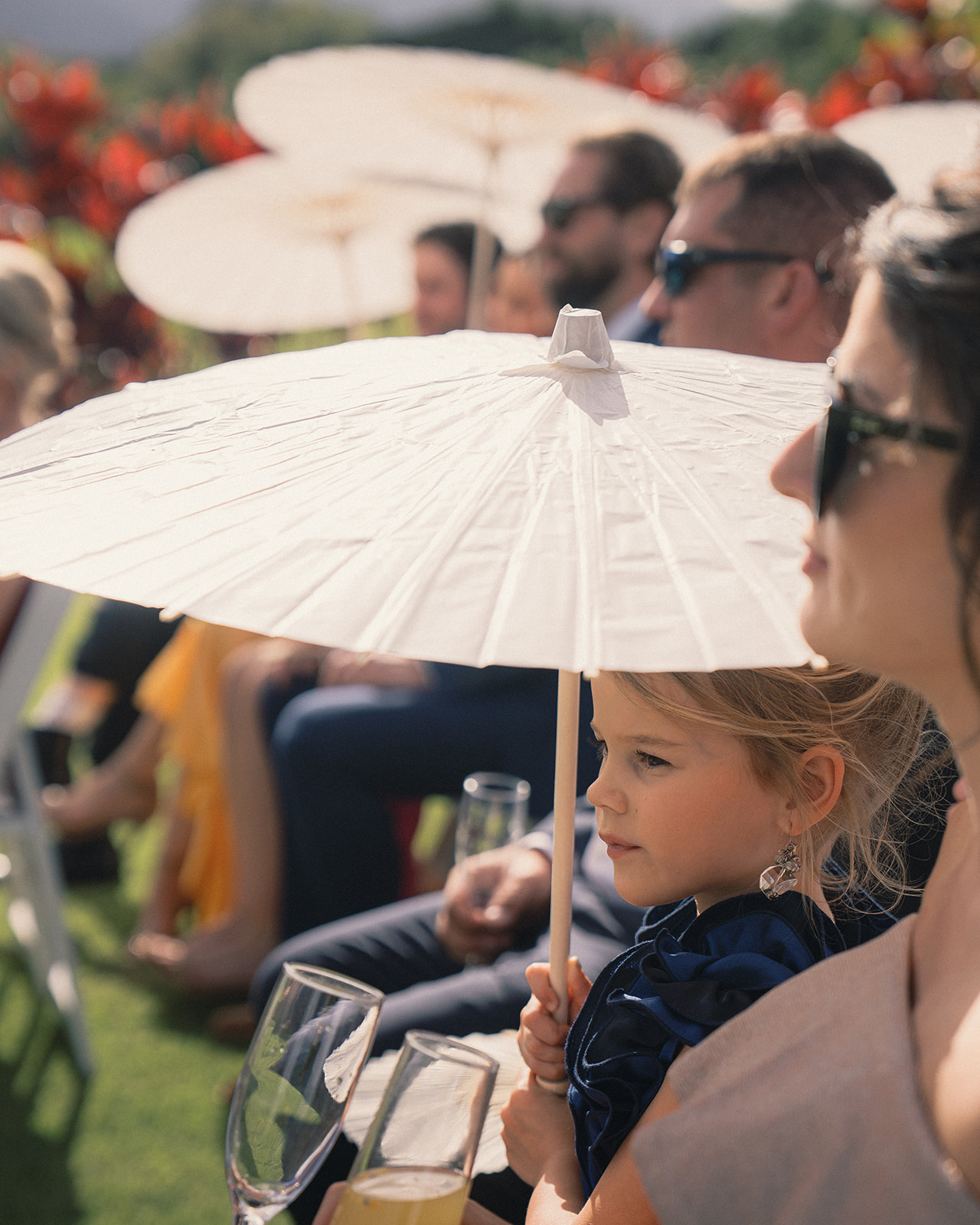 Young girl holding a parasol at a marriage proposal ceremony, with guests seated in the background, captured in Marriage Proposal Photo Session in Oahu.