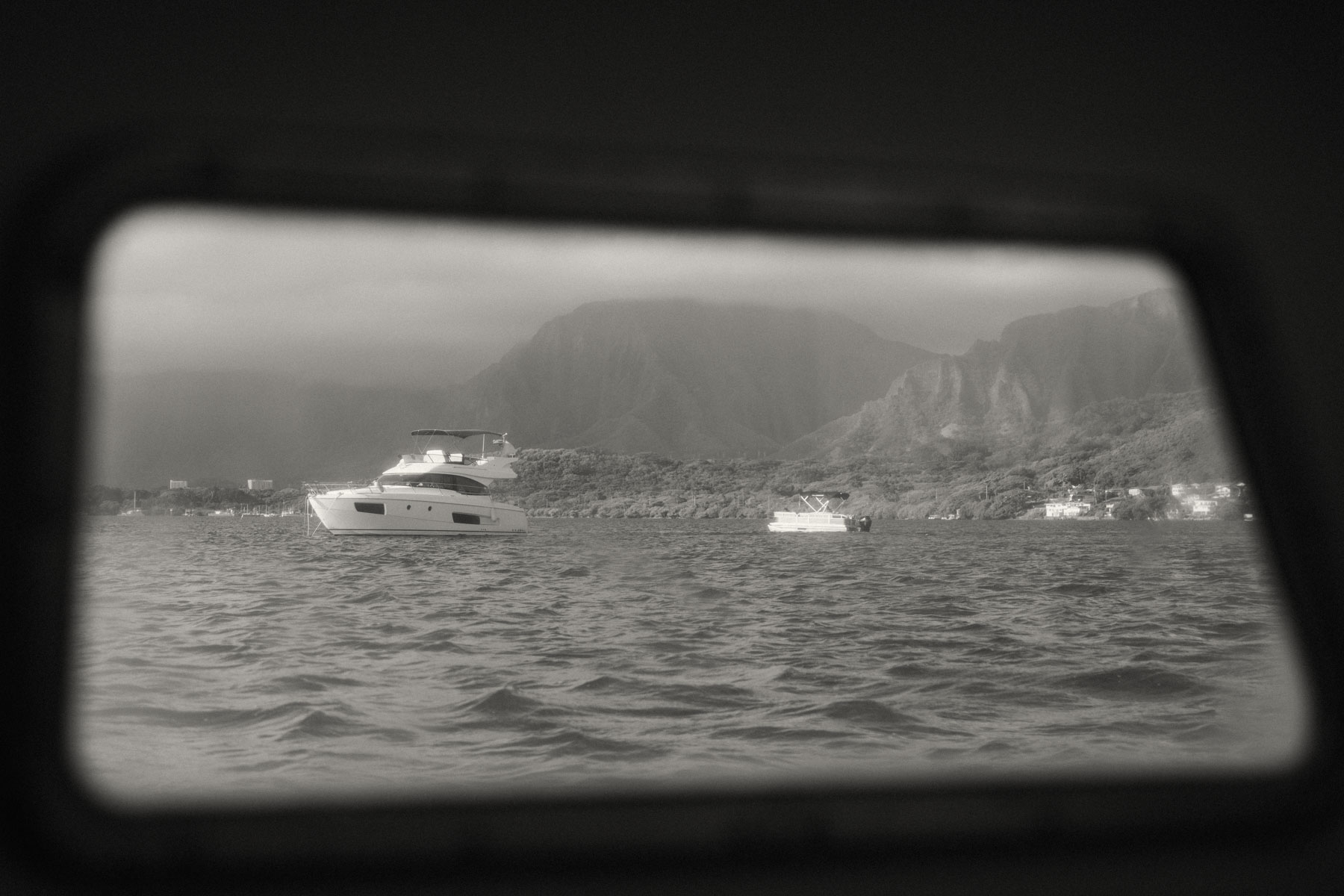 A serene, black-and-white shot of a couple on a boat, with the mountains in the background and a feeling of intimacy between them. The photo perfectly complements a Complete Photography Guide in Kaneohe.