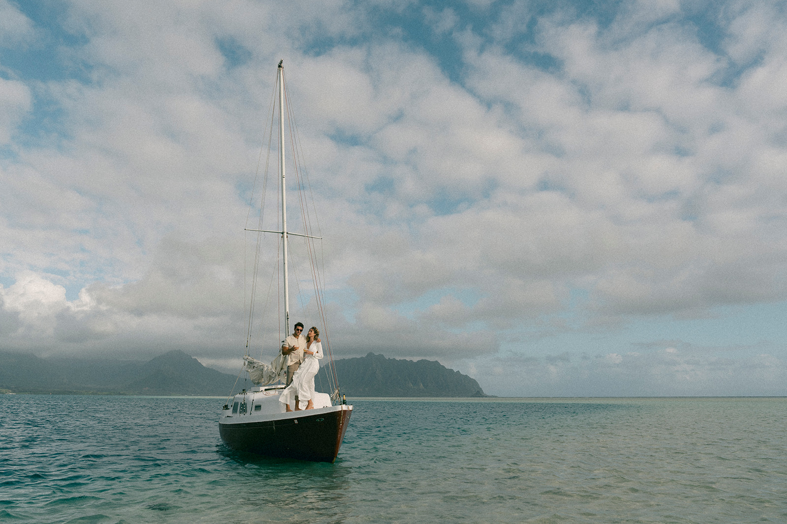 Couple celebrating their engagement aboard a sailboat in Oahu, surrounded by clear skies and calm waters in Marriage Proposal Photo Session in Oahu.