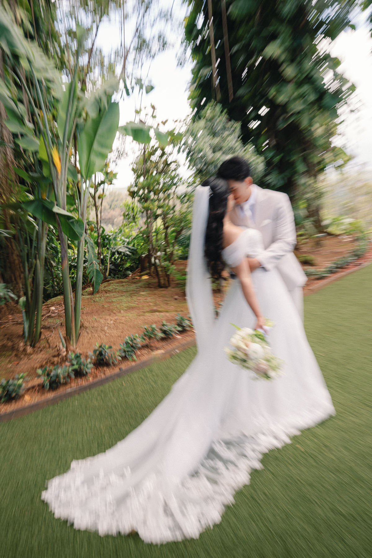 Bride and groom sharing a kiss as they walk through a lush garden, with the bride’s veil flowing, captured in Wedding Photography on Oahu.