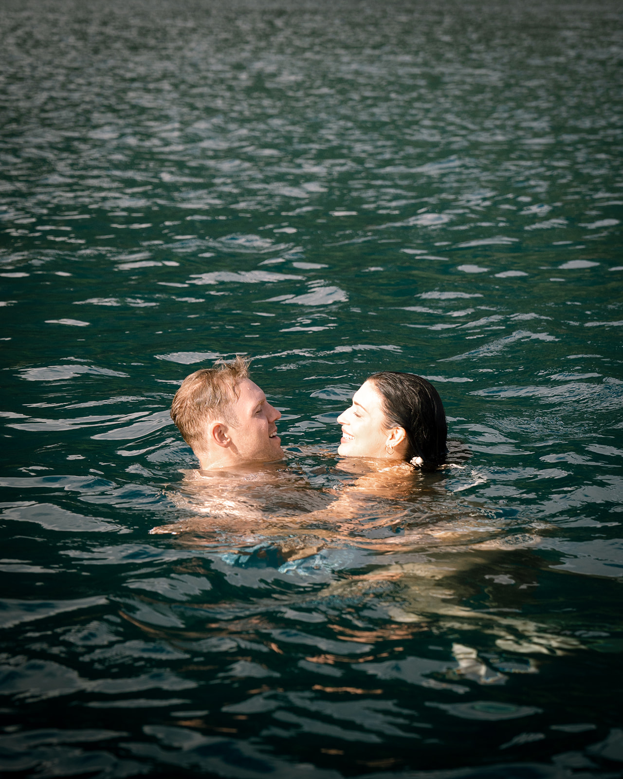 Groom and bride immersed in ocean water with lush cliffs behind – Top Questions to Ask Your Wedding Photographer Before Booking
