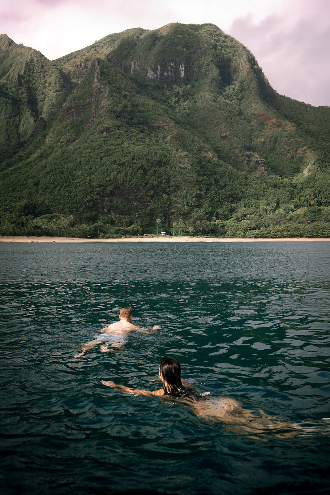 Couple swimming in tropical bay with lush green mountains – Top Questions to Ask Your Wedding Photographer Before Booking