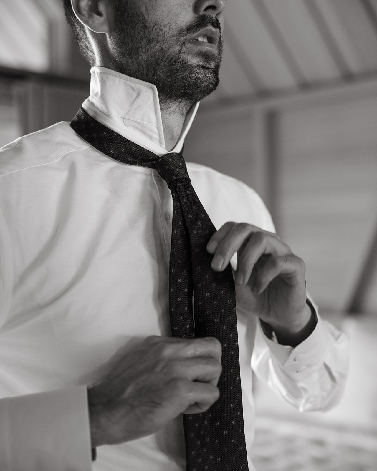 Groom tying textured tie indoors during Sunset Ranch wedding Oahu groom preparation