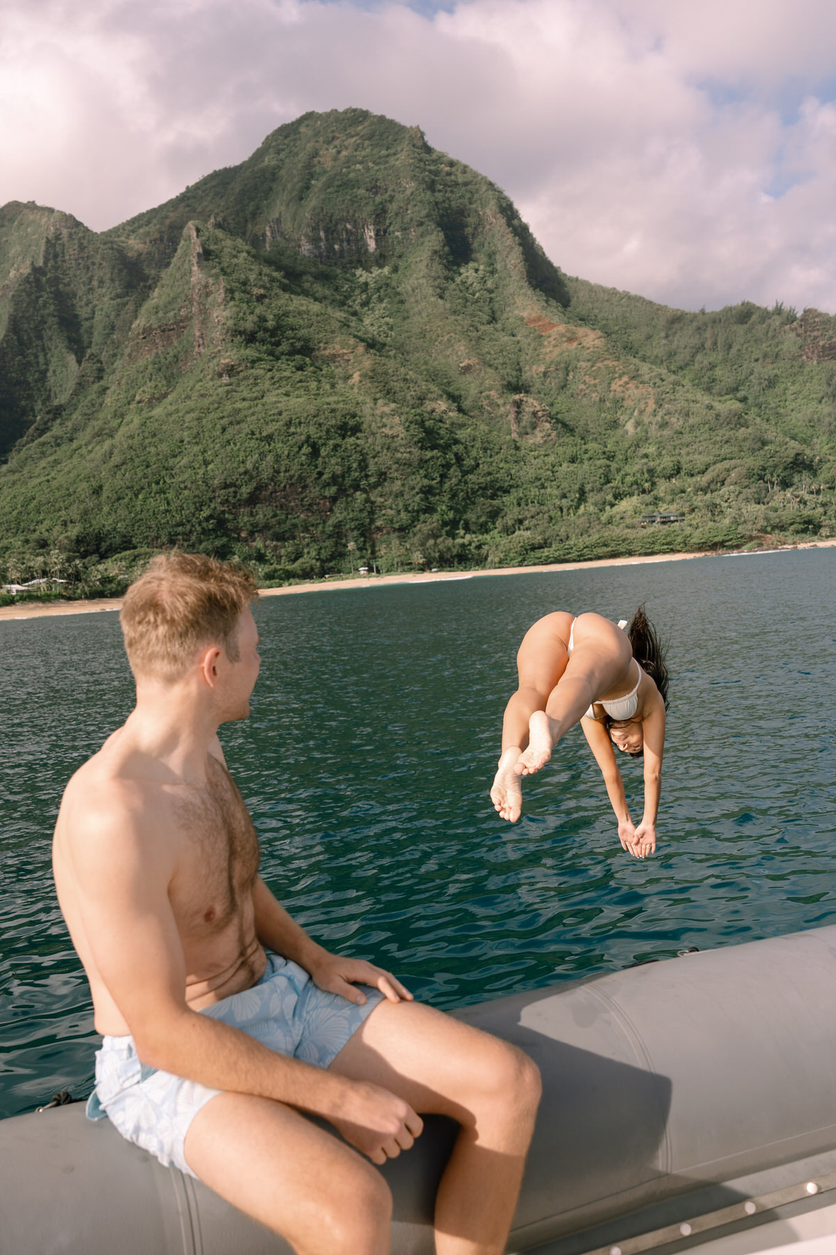 The bride prepares to dive into the clear waters from the boat as the groom watches her with a smile. This adventurous moment captures the fun and relaxed nature of a Kauai elopement, where couples can combine romantic moments with thrilling experiences like ocean dives.