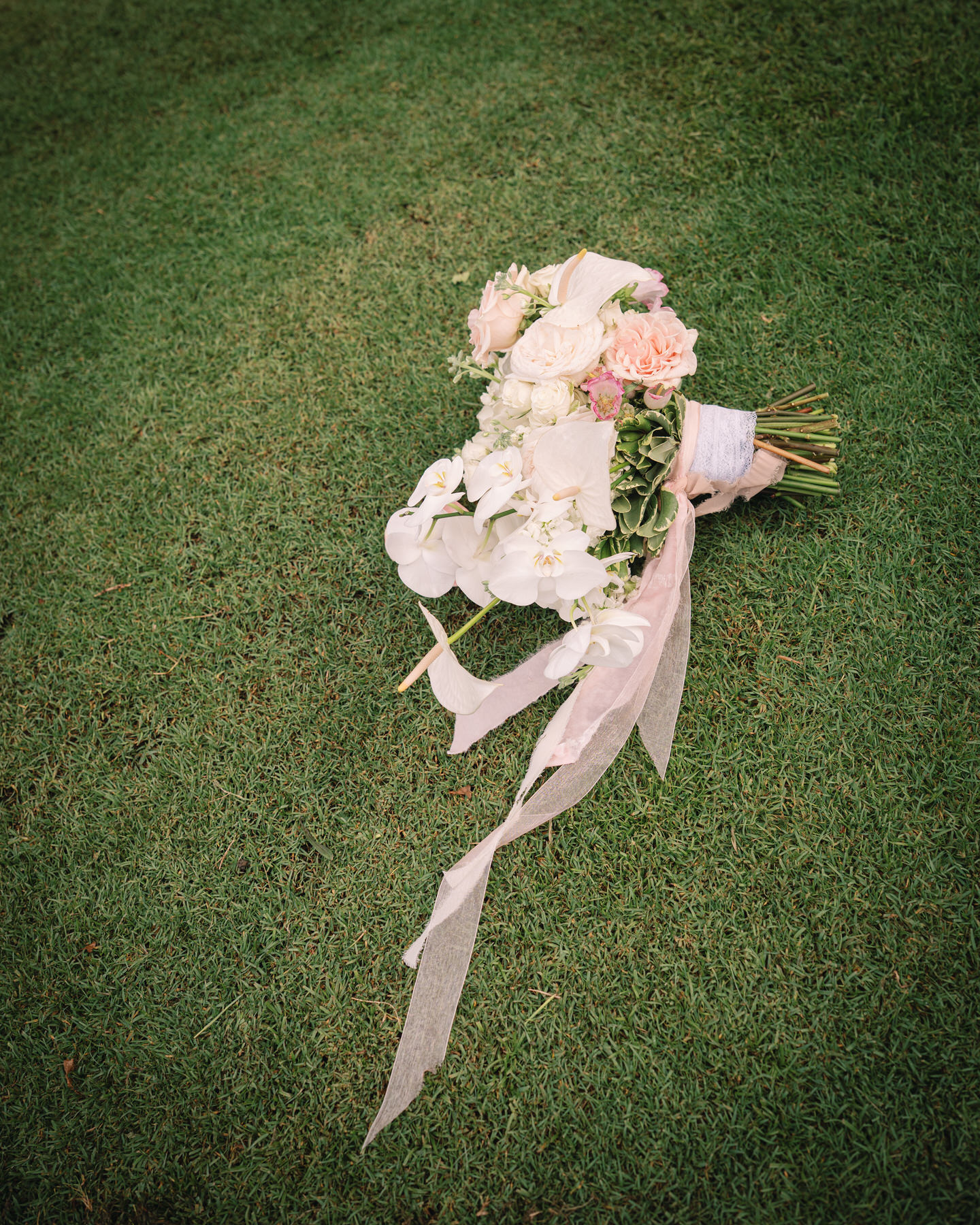 A beautifully arranged bridal bouquet, made up of soft pink and white flowers, lies on the grass. This simple yet elegant bouquet captures the delicate details you can expect when planning your Kauai elopement, ensuring a personal and intimate touch to your ceremony.