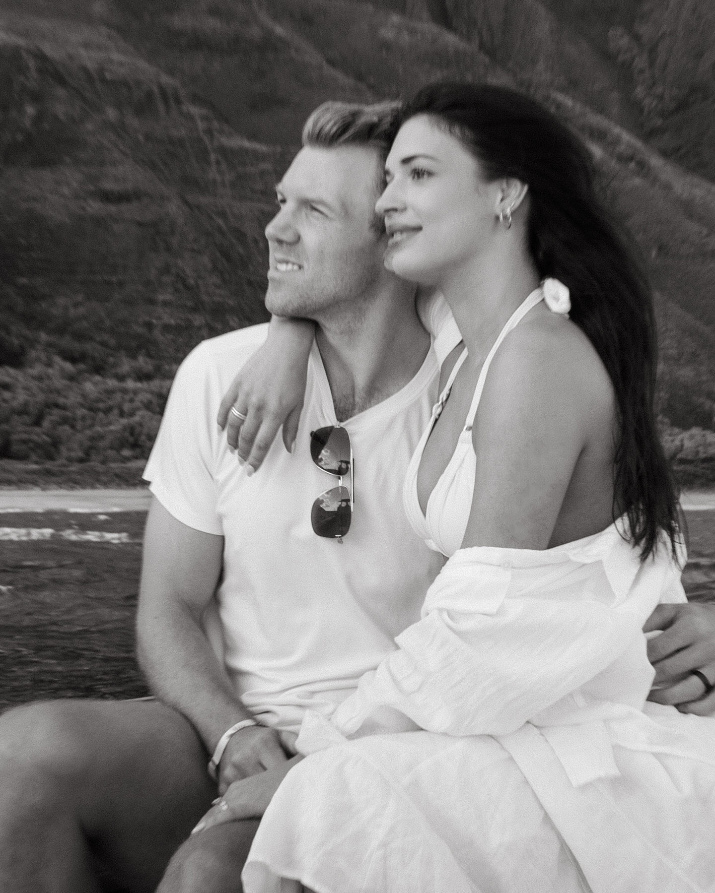 In a black-and-white photo, a couple gazes out over a picturesque Kauai backdrop, with the woman resting her head on her partner’s shoulder. This moment of intimacy captures the essence of a Kauai elopement, highlighting the quiet, peaceful moments you can enjoy when planning a private wedding in paradise.