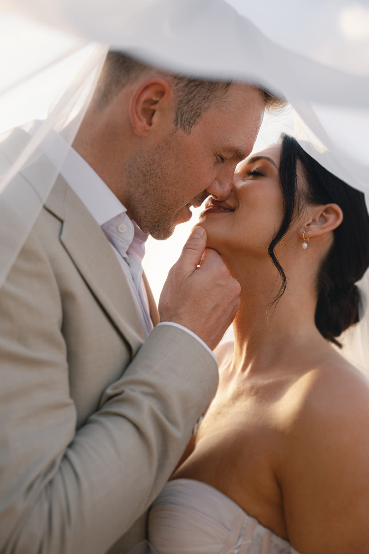 A close-up of the bride and groom, sharing a kiss under the veil during their Kauai elopement ceremony. The soft, golden light from the sunset highlights their connection and the intimate nature of eloping in Kauai, a perfect way to celebrate your love.