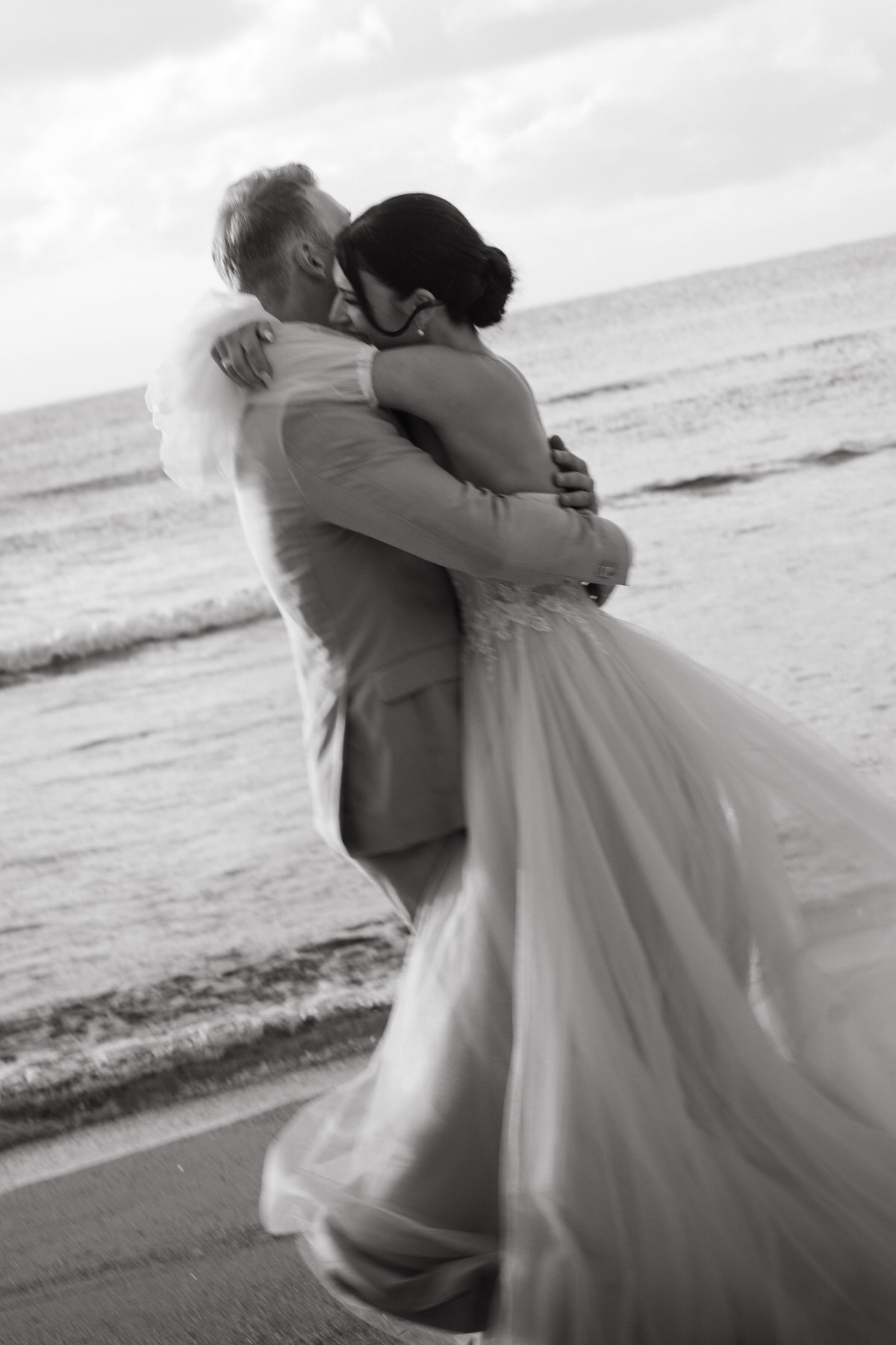 The bride and groom share an elegant and passionate embrace during their Kauai elopement. The backdrop of the beach and waves crashing gently along the shore underscores the romantic and intimate atmosphere that Kauai provides for an unforgettable elopement.