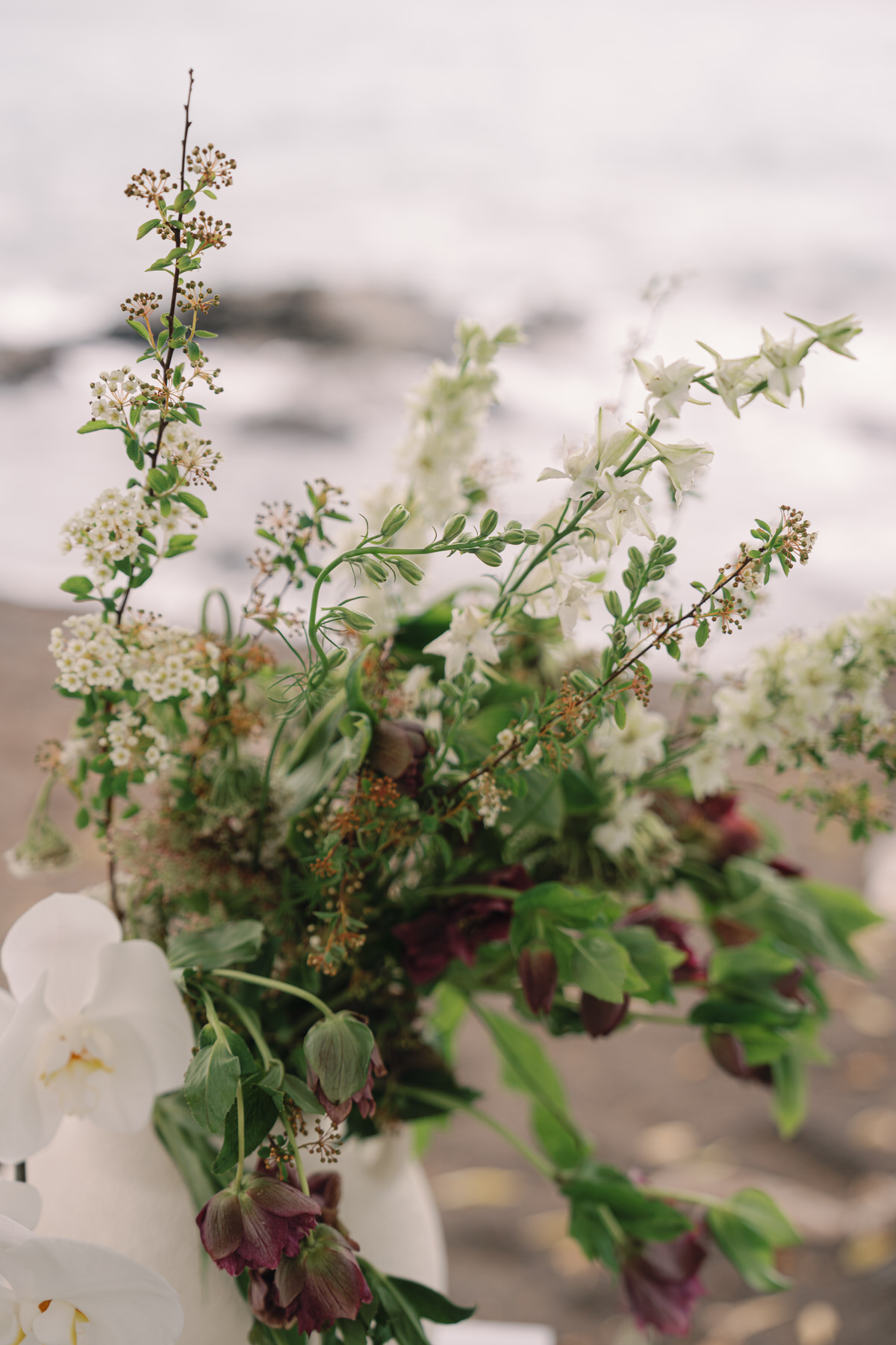 A close-up of a beautiful floral arrangement featuring a mix of white flowers and greenery. The arrangement sits elegantly on a table near the ocean, highlighting the tranquil beauty of Oahu’s coastline. This serene setting emphasizes the importance of hiring your Oahu wedding vendors early to secure stunning floral designs (and my personal recommendations).