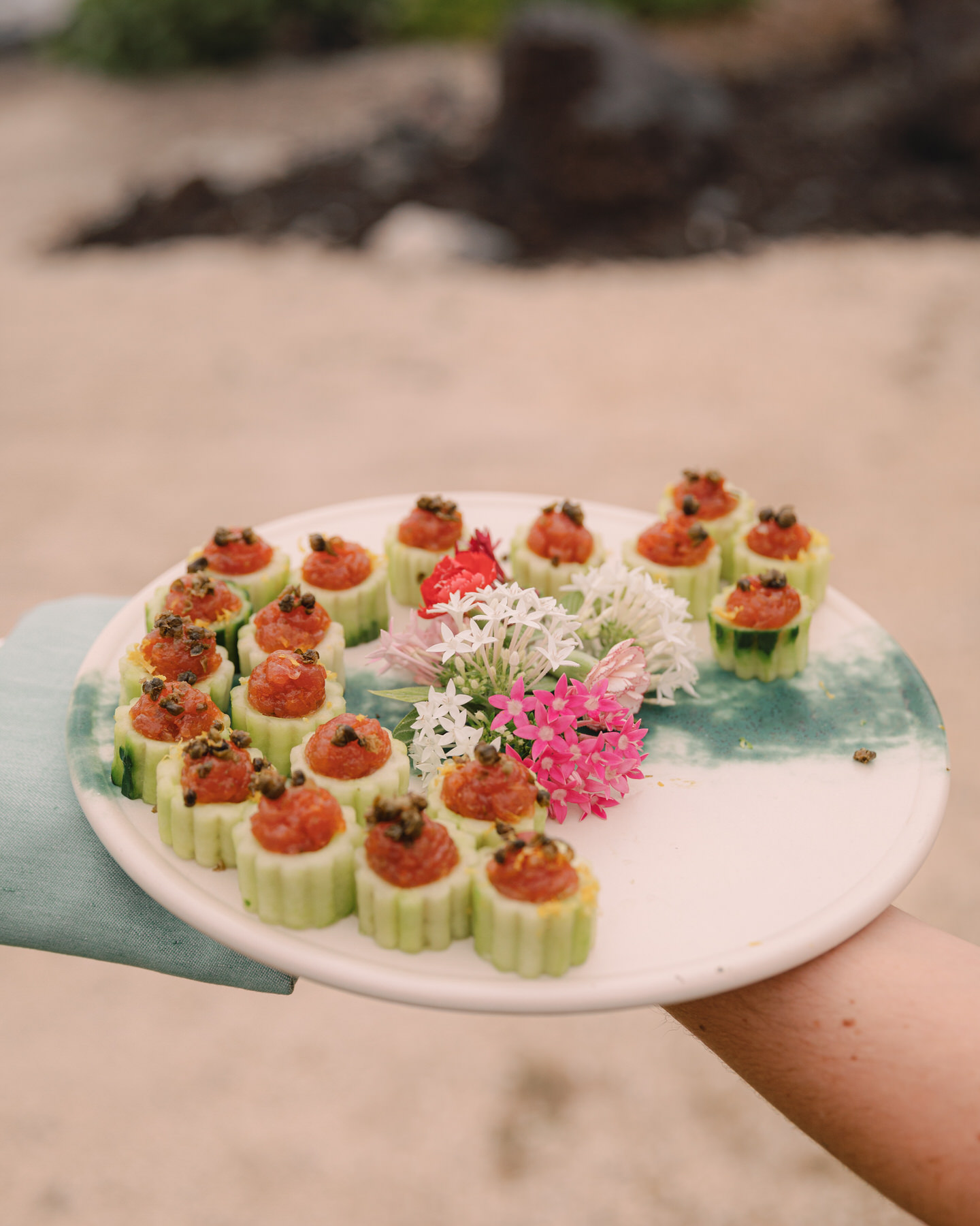 A plate of elegantly presented cucumber cups filled with fresh salmon tartare, garnished with edible flowers, is offered to guests at a wedding reception. This beautifully crafted dish serves as an example of why it's vital to hire top-tier Oahu wedding vendors early to secure exceptional catering options for your wedding (and my personal recommendations).